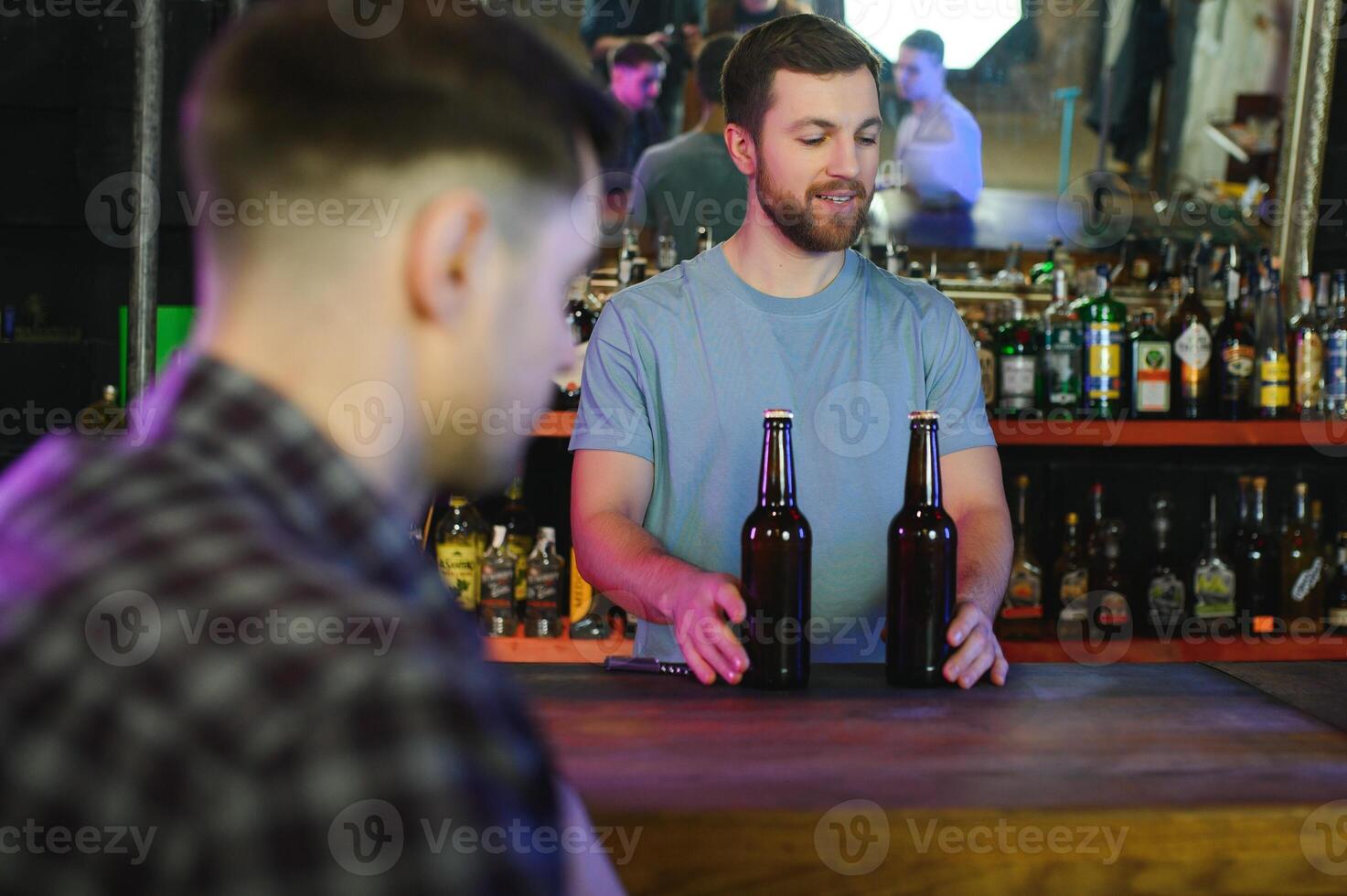 Barman bottle of beer. Nearby empty glass on wooden bar counter in interior of pub, cropped, free space. photo