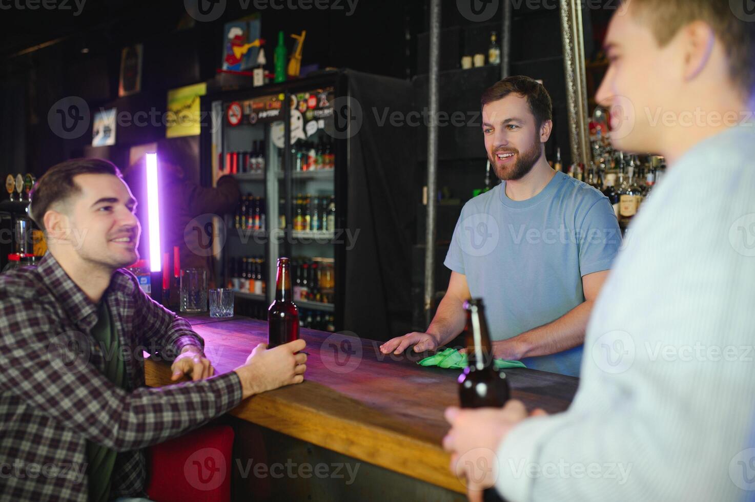 Two young men in casual clothes are smiling and talking while sitting at bar counter in pub photo