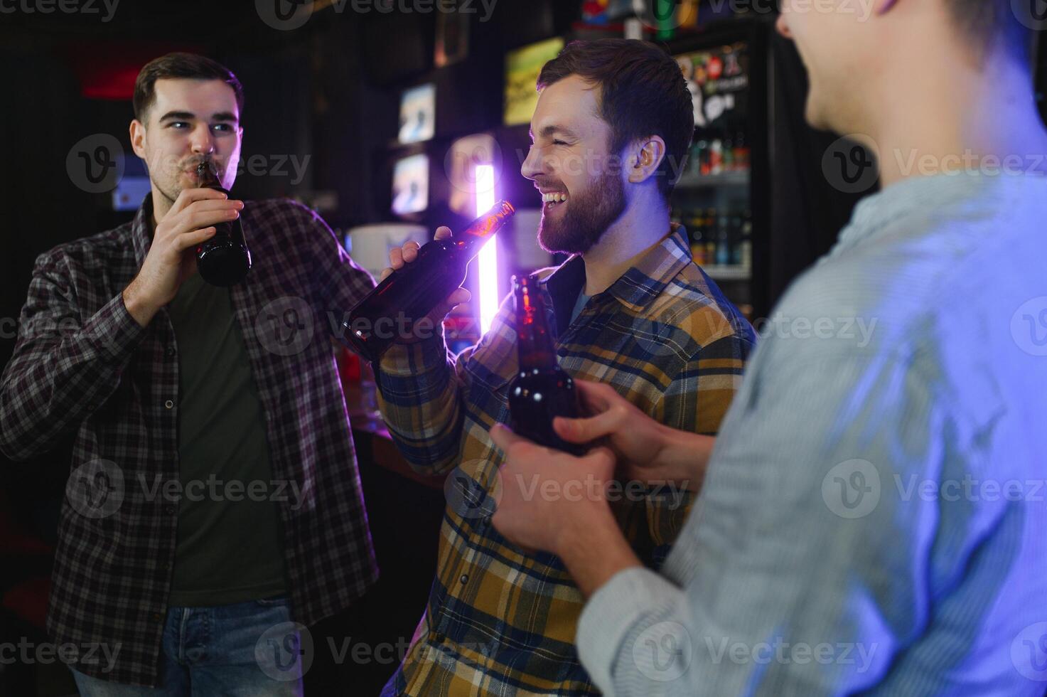 Young men in casual clothes are talking, laughing and drinking while sitting at bar counter in pub photo