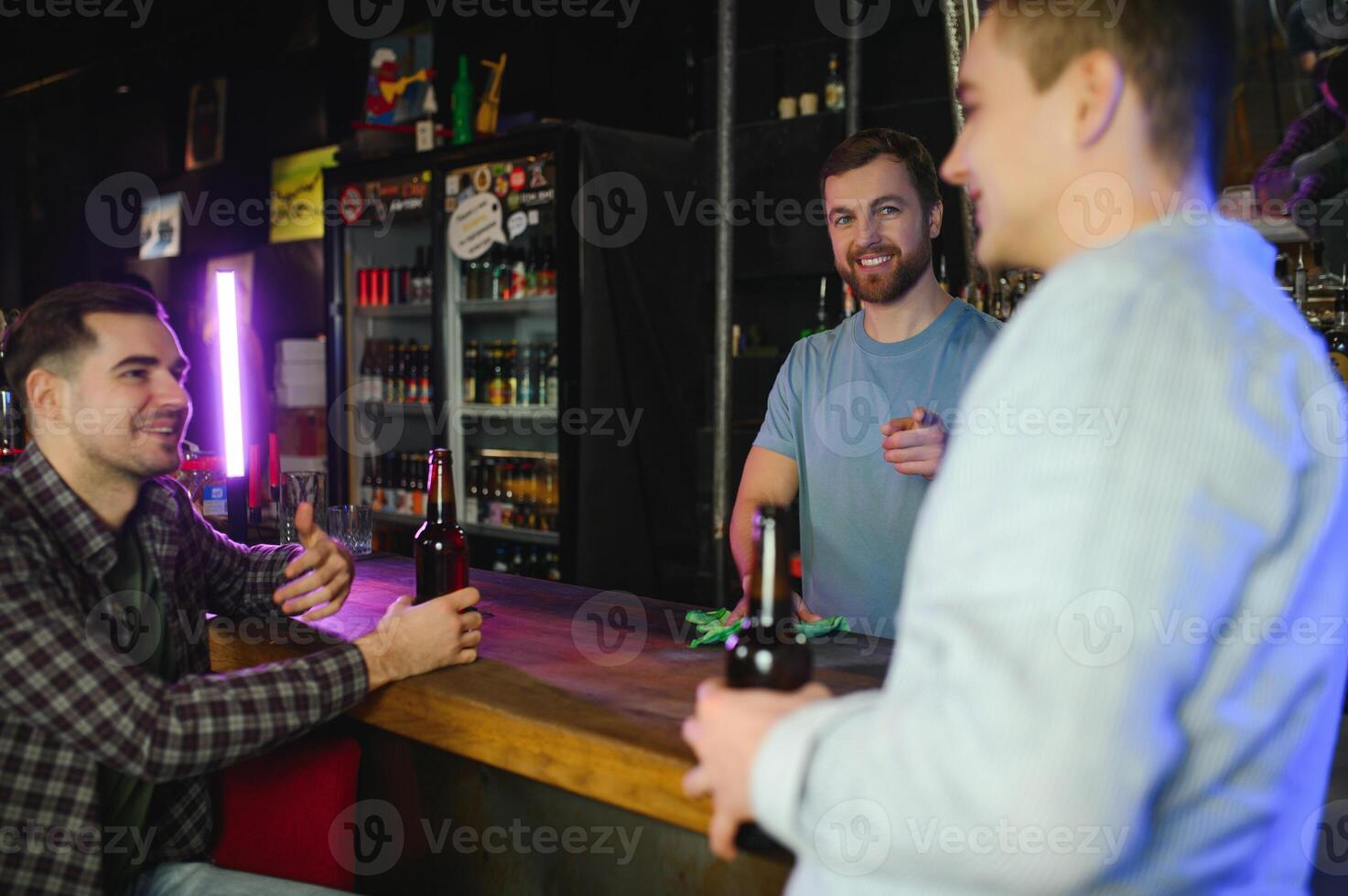 Two young men in casual clothes are smiling and talking while sitting at bar counter in pub photo