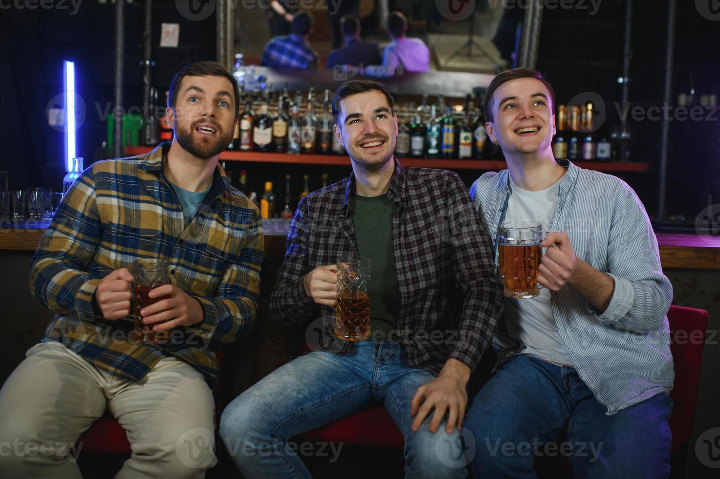Young men in casual clothes are talking, laughing and drinking while sitting at bar counter in pub photo
