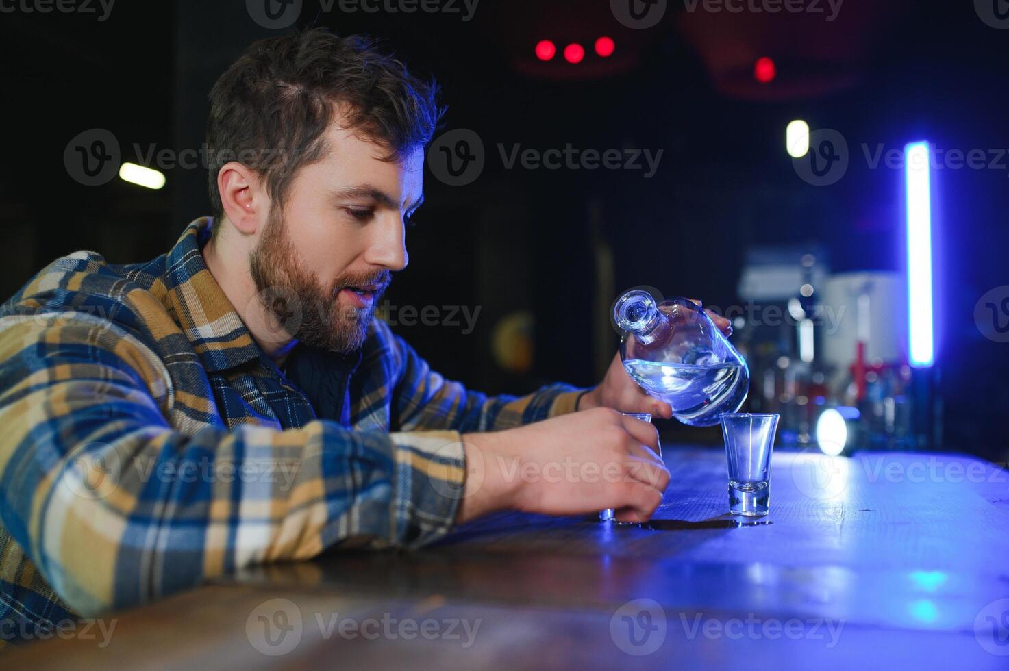 Sad young man sitting at bar counter in pub. Upset man drinks alcohol because of problems at work. photo