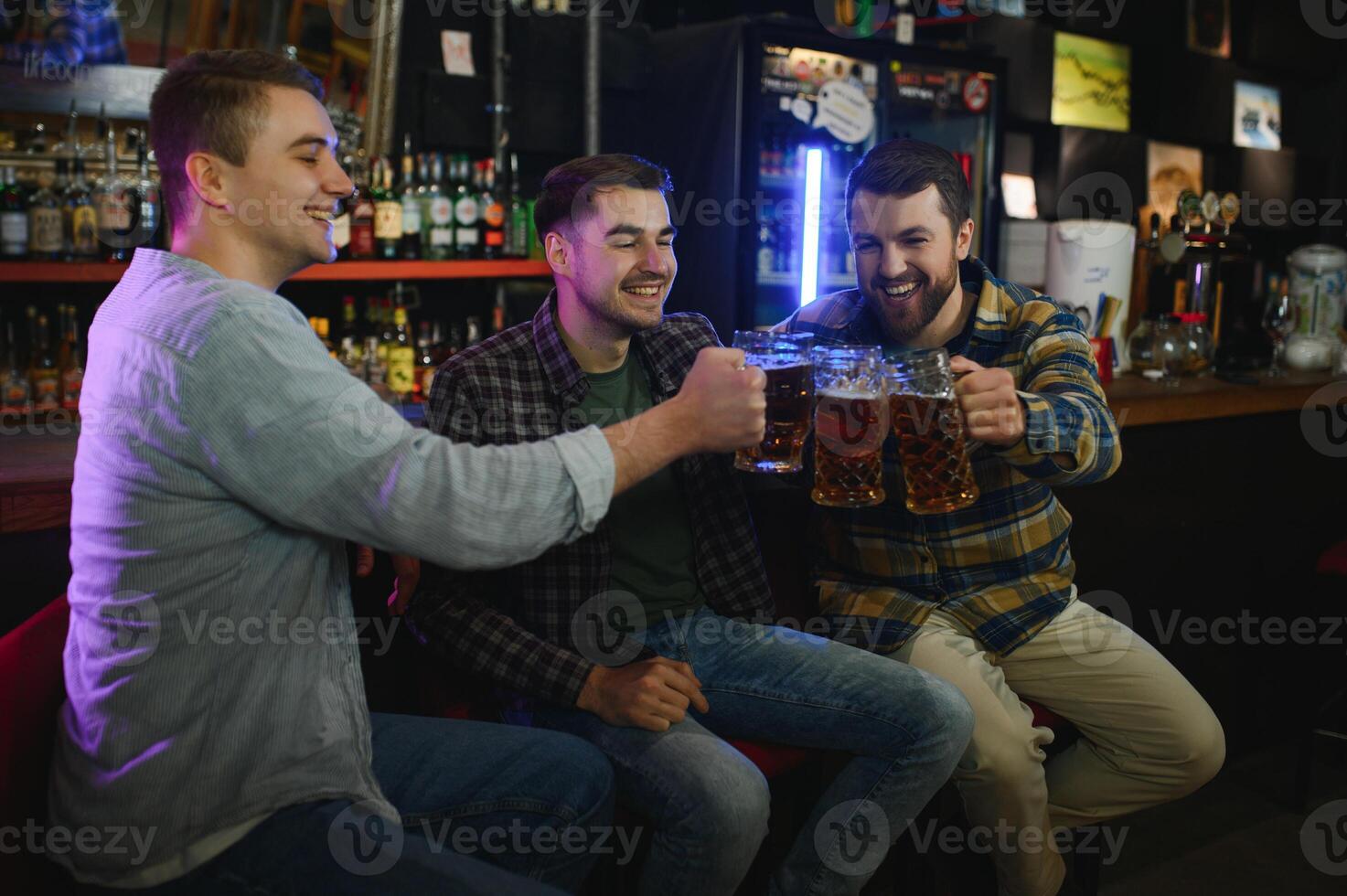Old friends meeting. Happy young men in casual wear toasting with beer while sitting in beer pub together photo