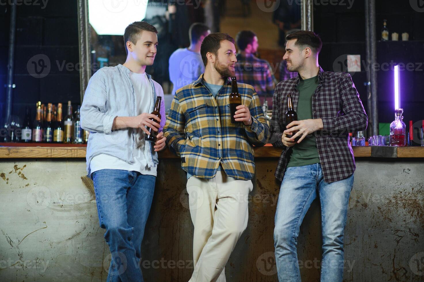 Young men in casual clothes are talking, laughing and drinking while sitting at bar counter in pub photo