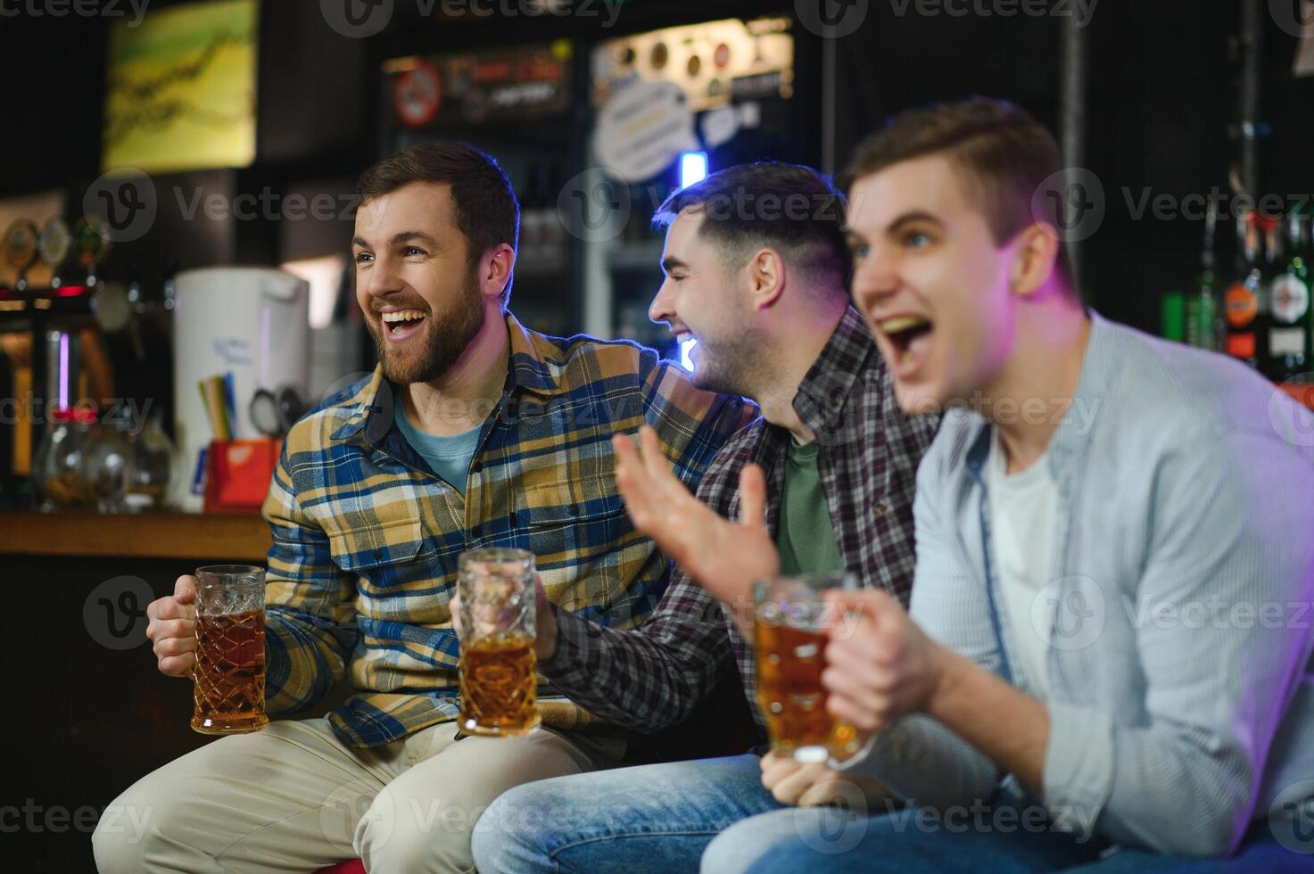 Soccer fans cheering for favourite team while enjoying drinks. Group of supporters celebrating victory while watching football match on tv in a club. Happy friends shouting while cheering for a goal. photo