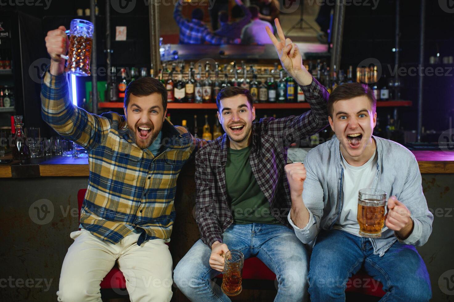 Soccer fans cheering for favourite team while enjoying drinks. Group of supporters celebrating victory while watching football match on tv in a club. Happy friends shouting while cheering for a goal. photo