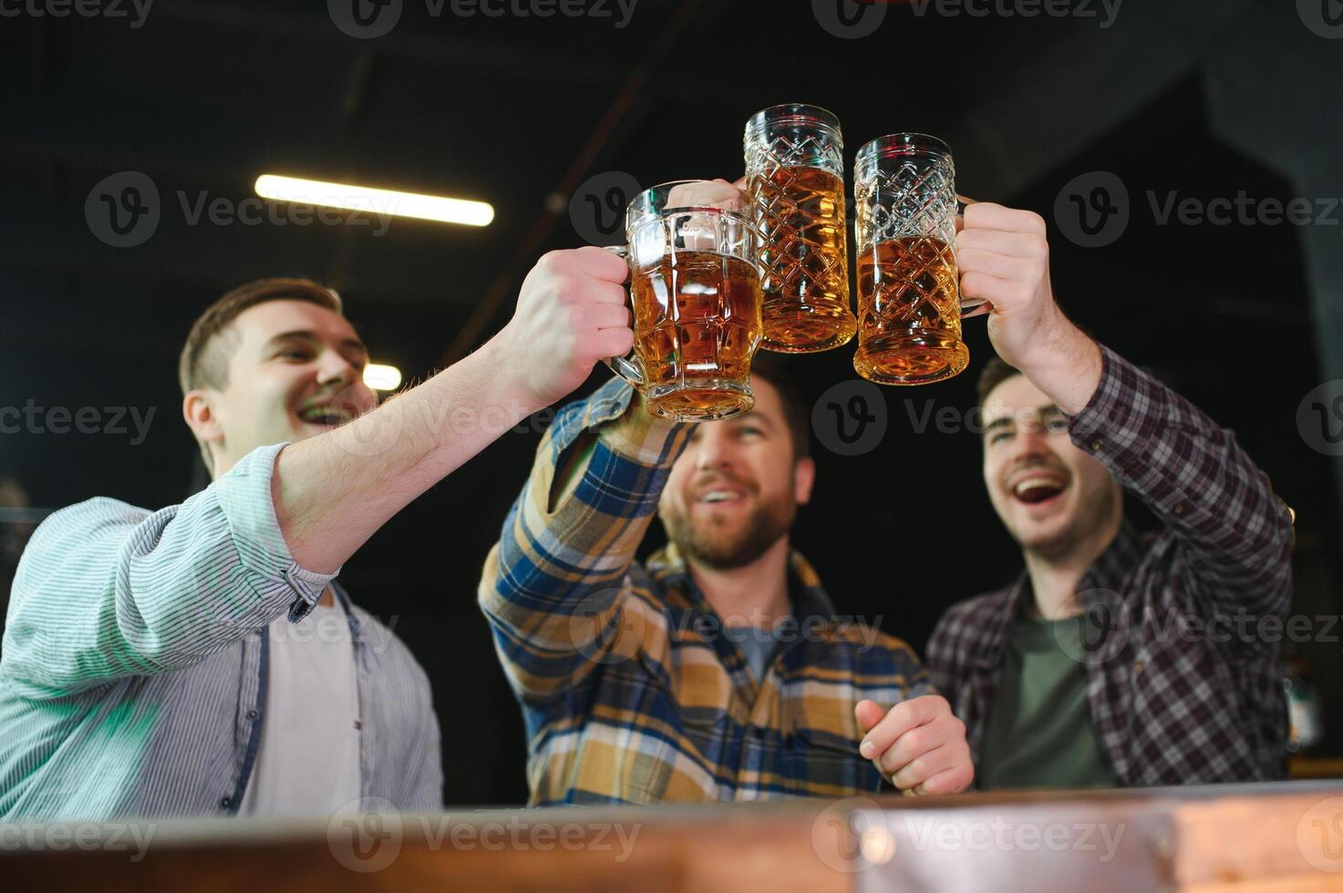 Soccer fans cheering for favourite team while enjoying drinks. Group of supporters celebrating victory while watching football match on tv in a club. Happy friends shouting while cheering for a goal. photo