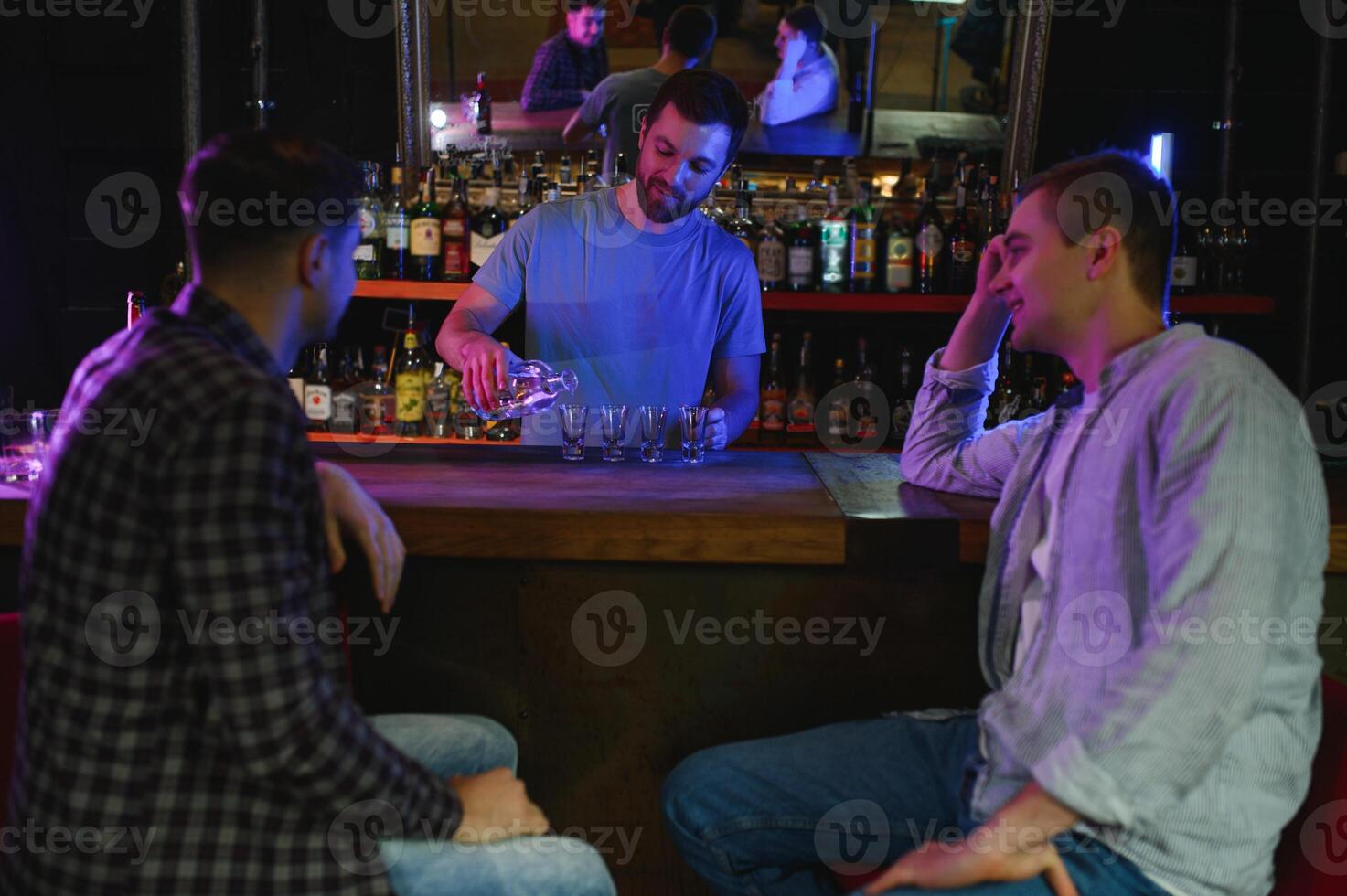 Two young men in casual clothes are smiling and talking while sitting at bar counter in pub photo