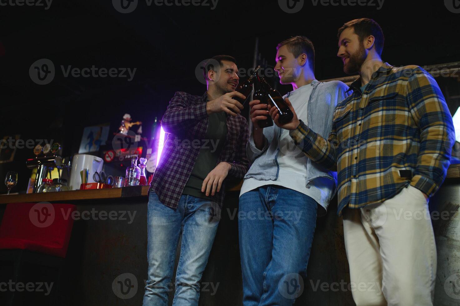 Young men in casual clothes are talking, laughing and drinking while sitting at bar counter in pub photo