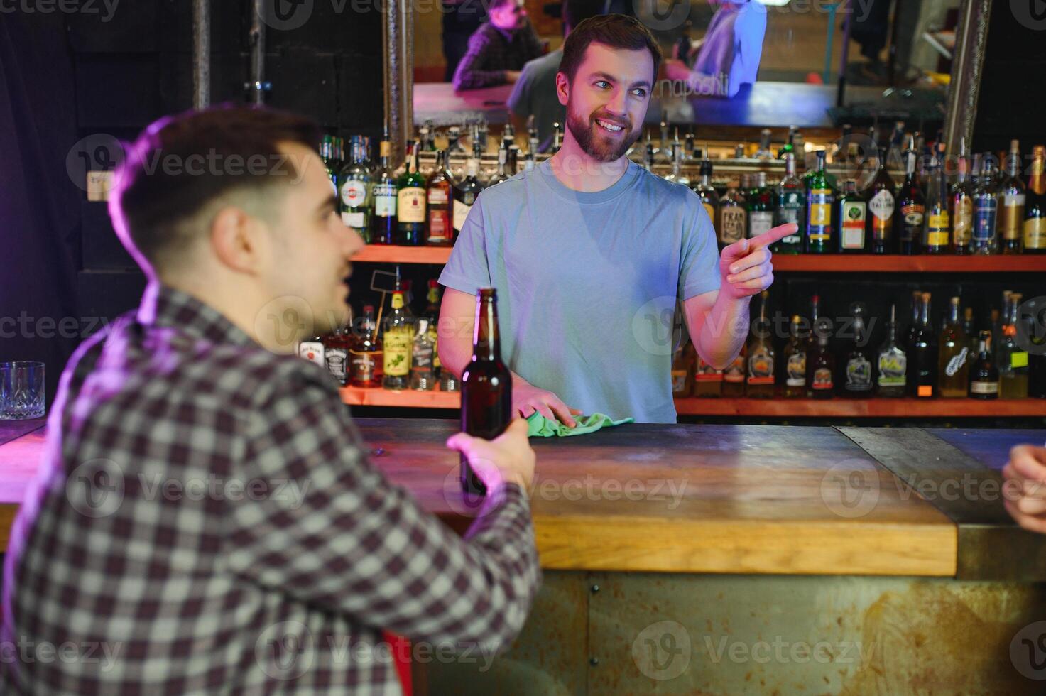 Barman bottle of beer. Nearby empty glass on wooden bar counter in interior of pub, cropped, free space. photo