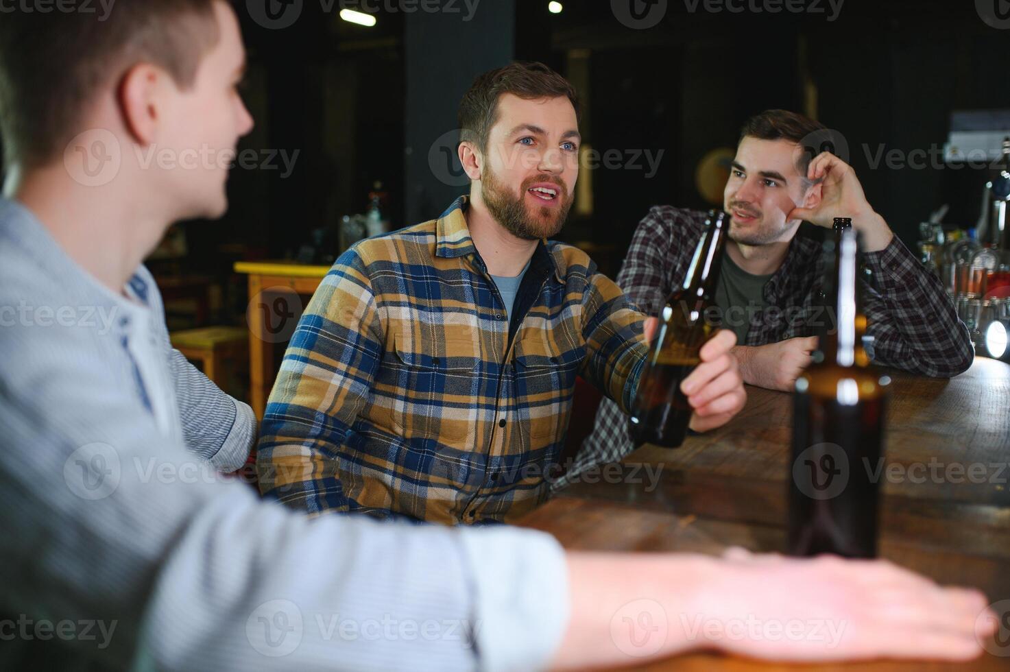 Young men in casual clothes are talking, laughing and drinking while sitting at bar counter in pub photo