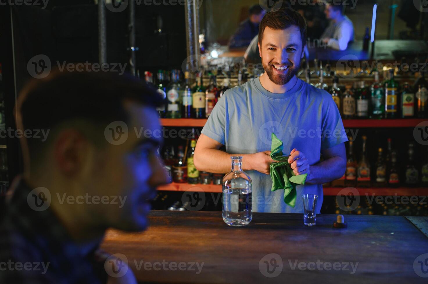 Barman pouring hard spirit into glasses for two male friends relaxing in a bar photo