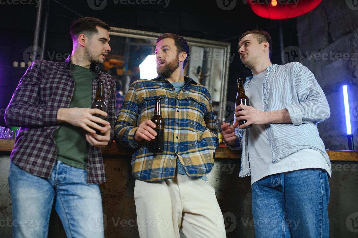 Young men in casual clothes are talking, laughing and drinking while sitting at bar counter in pub photo