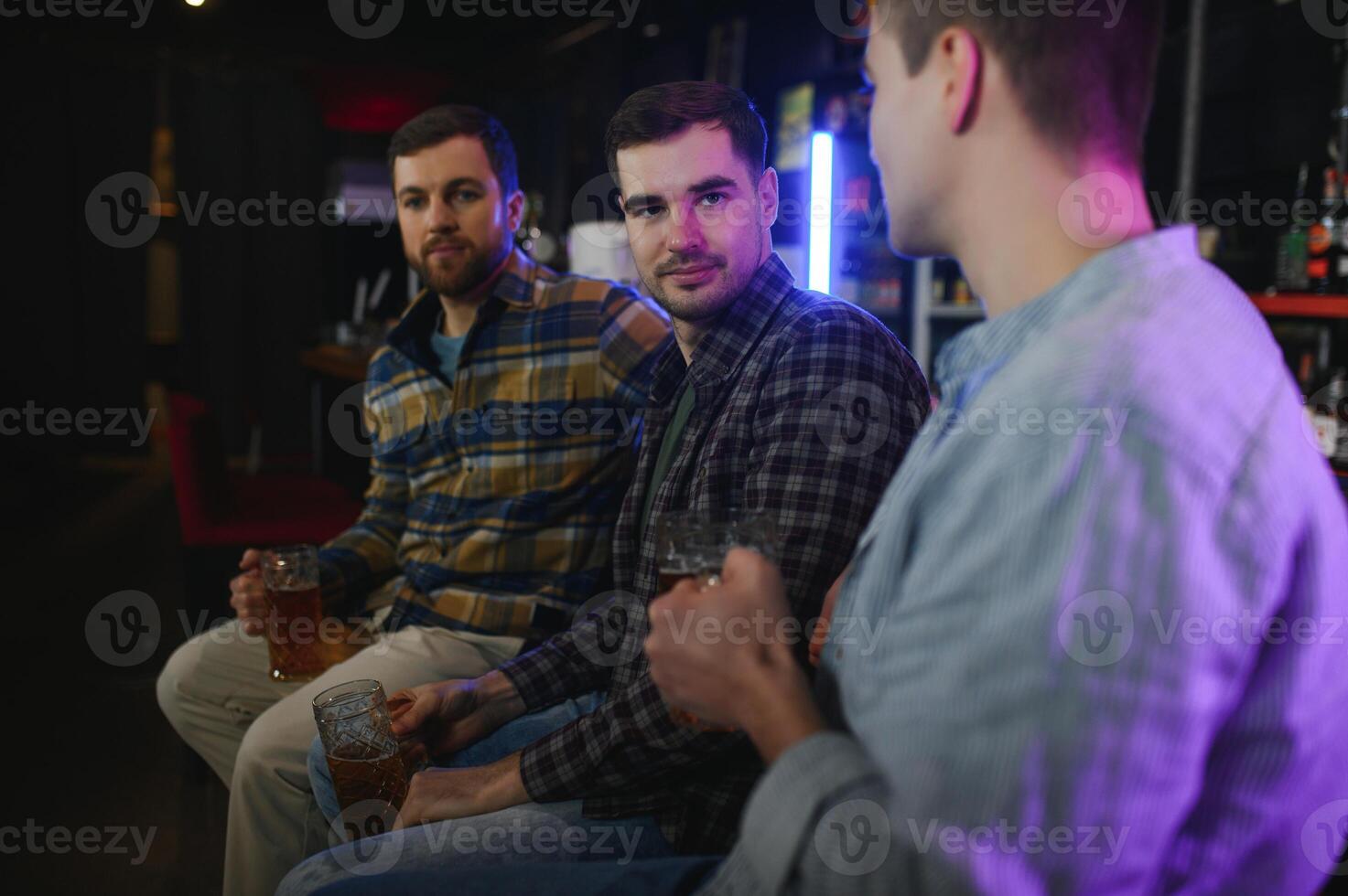 Old friends meeting. Happy young men in casual wear toasting with beer while sitting in beer pub together photo