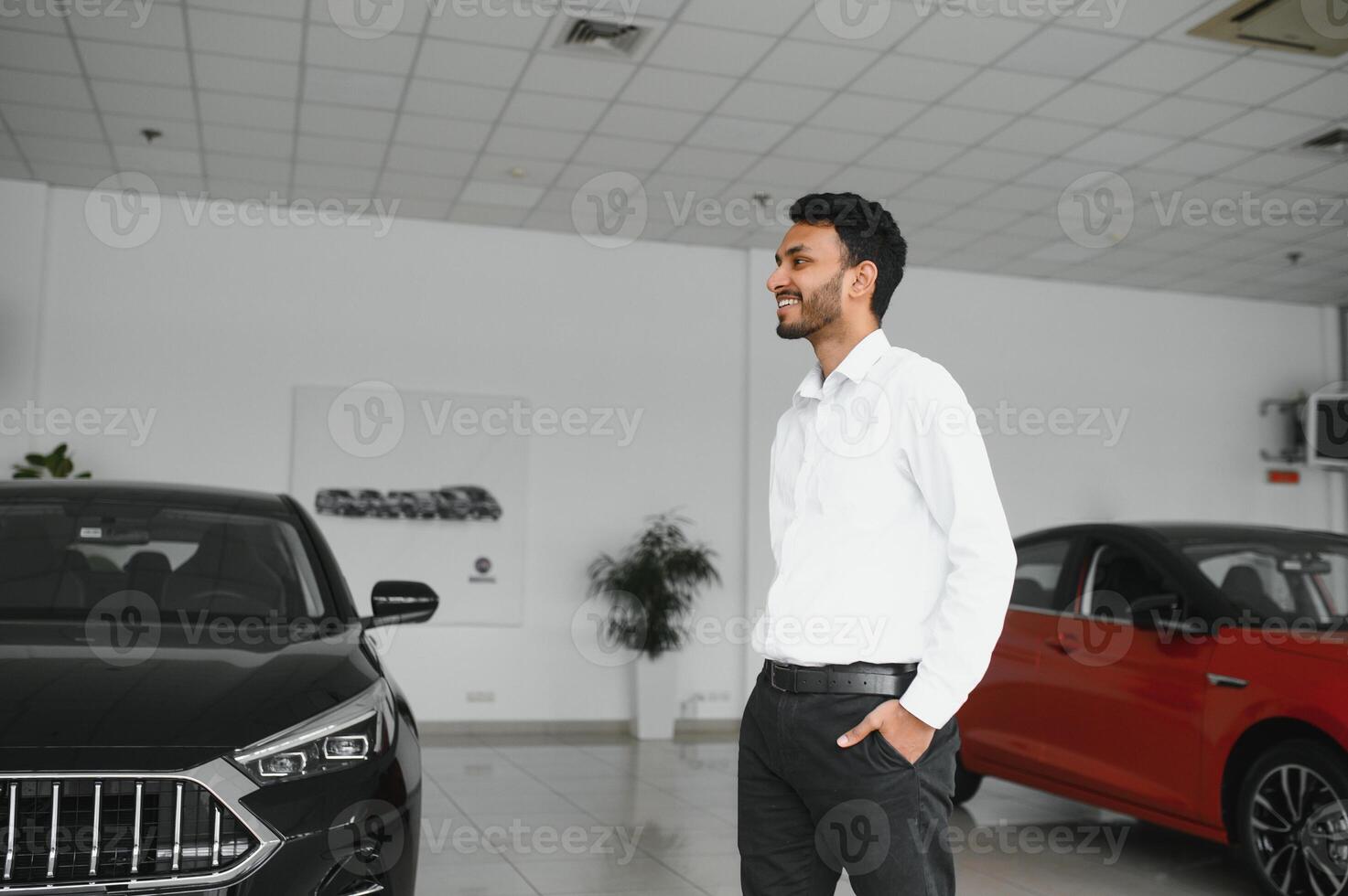Good looking, cheerful and friendly indian salesman poses in a car salon or showroom. photo