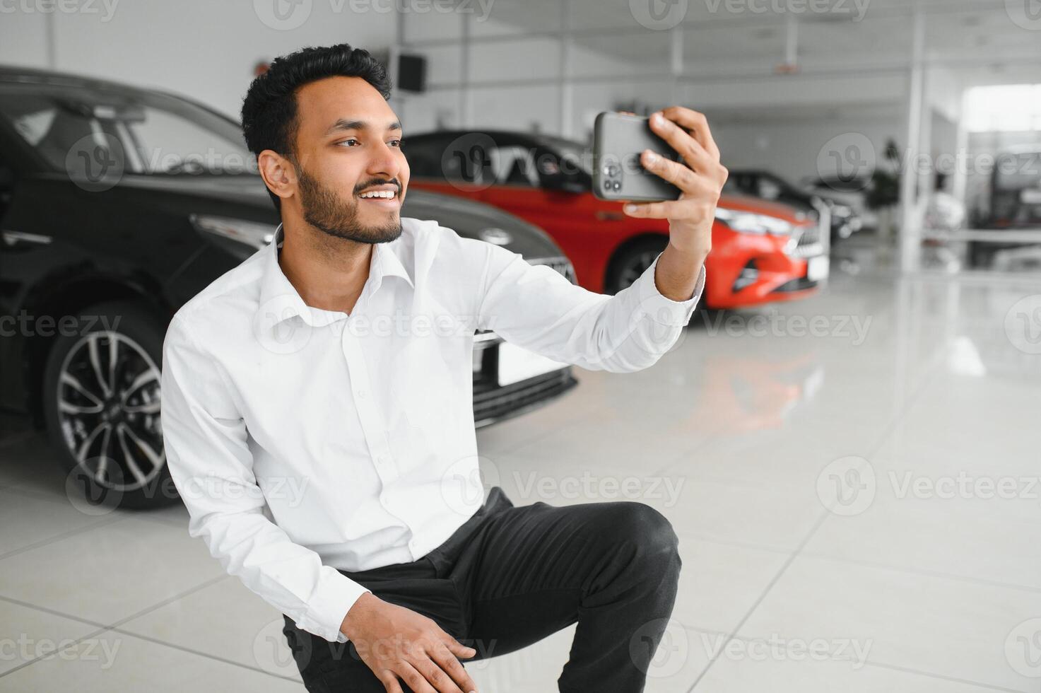 Handsome indian man taking a selfie with car keys to his new automobile at the dealership showroom copyspace technology social media sharing positivity lifestyle travelling tourism. photo