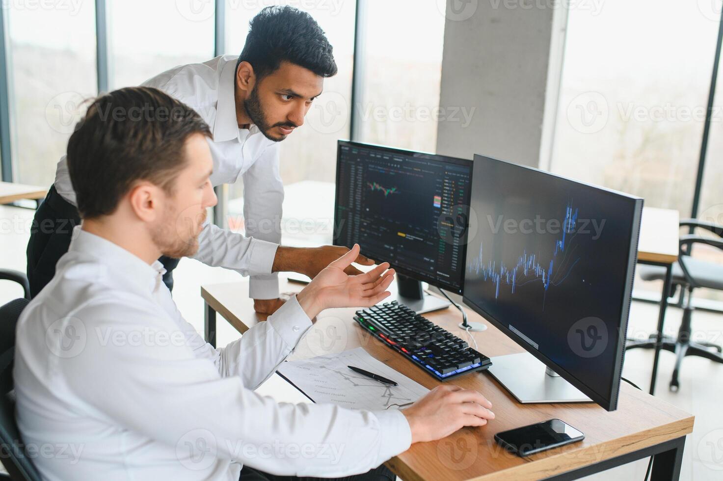 Two successful trader sitting in office and looking at screen, checking cryptocurrency information data on finance market graph, pointing on monitor photo