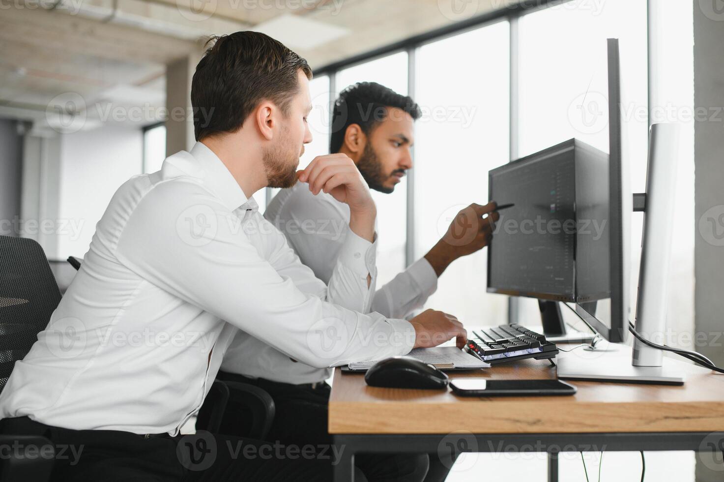 Two successful trader sitting in office and looking at screen, checking cryptocurrency information data on finance market graph, pointing on monitor photo