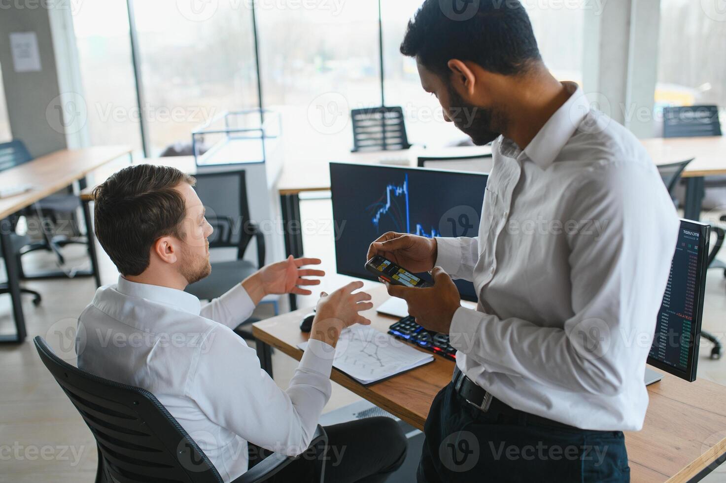 Two men traders sitting at desk at office together monitoring stocks data candle charts on screen analyzing price flow smiling cheerful having profit teamwork concept photo