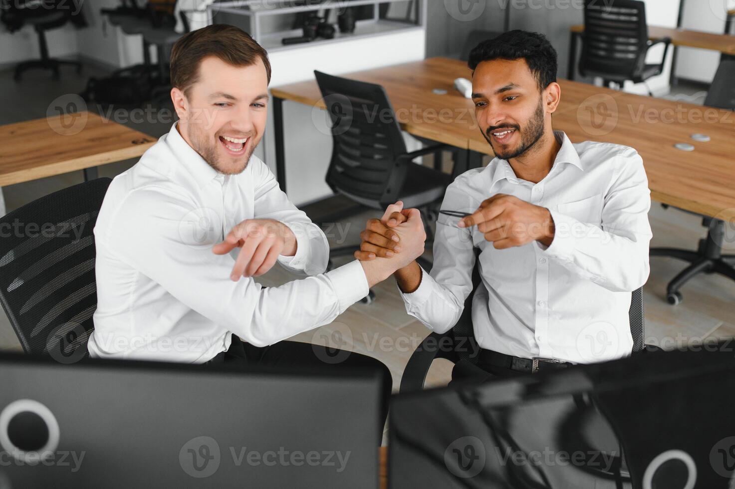 Two men traders sitting at desk at office together monitoring stocks data candle charts on screen analyzing price flow smiling cheerful having profit teamwork concept photo