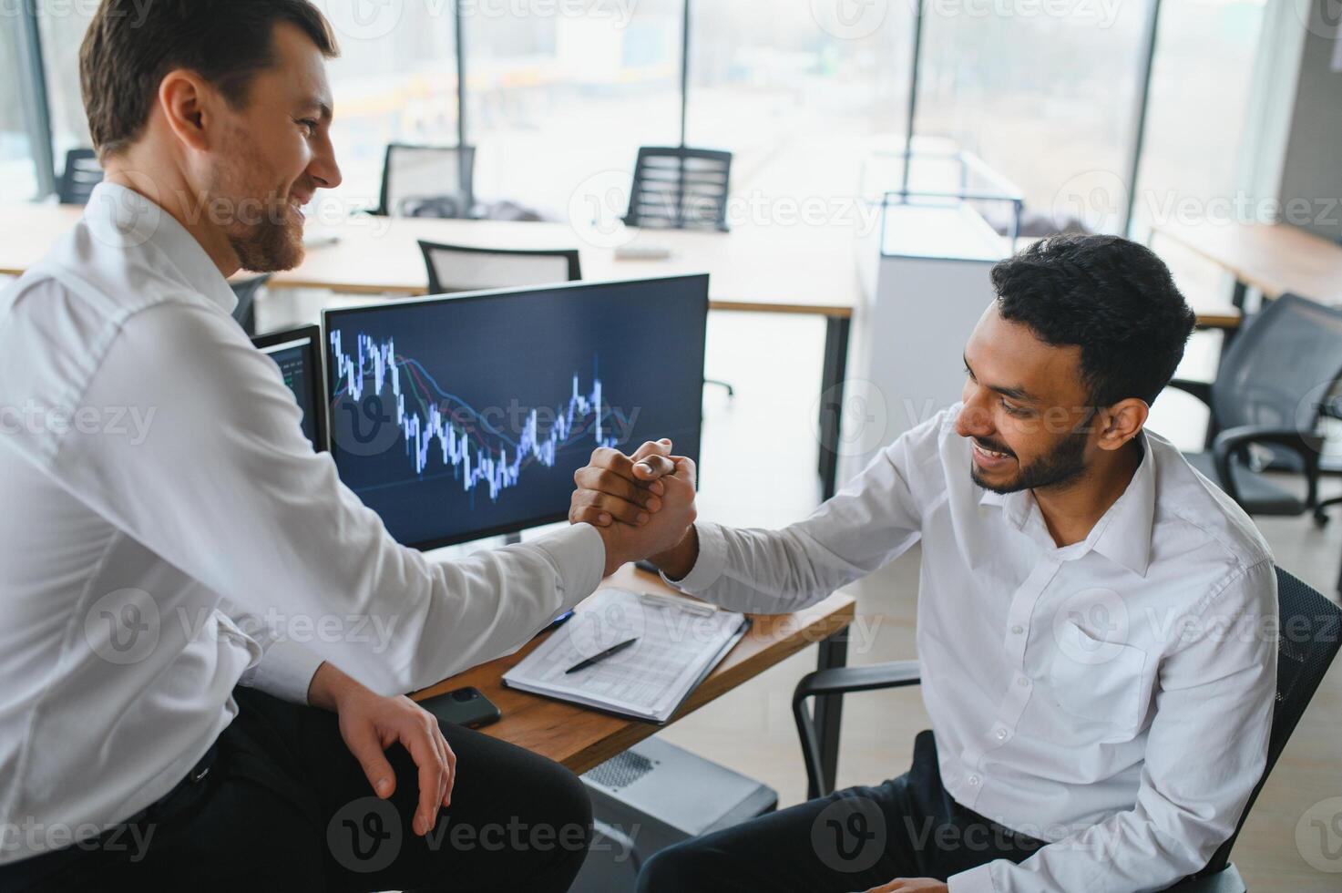 Two successful trader sitting in office and looking at screen, checking cryptocurrency information data on finance market graph, pointing on monitor photo