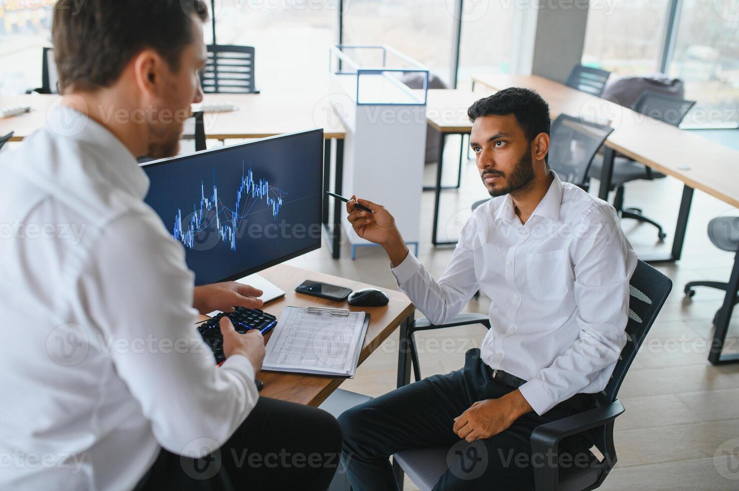 Two successful trader sitting in office and looking at screen, checking cryptocurrency information data on finance market graph, pointing on monitor photo