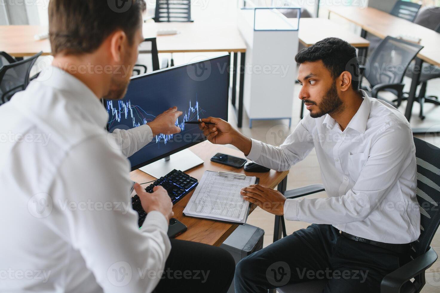 Two men traders sitting at desk at office together monitoring stocks data candle charts on screen analyzing price flow smiling cheerful having profit teamwork concept photo