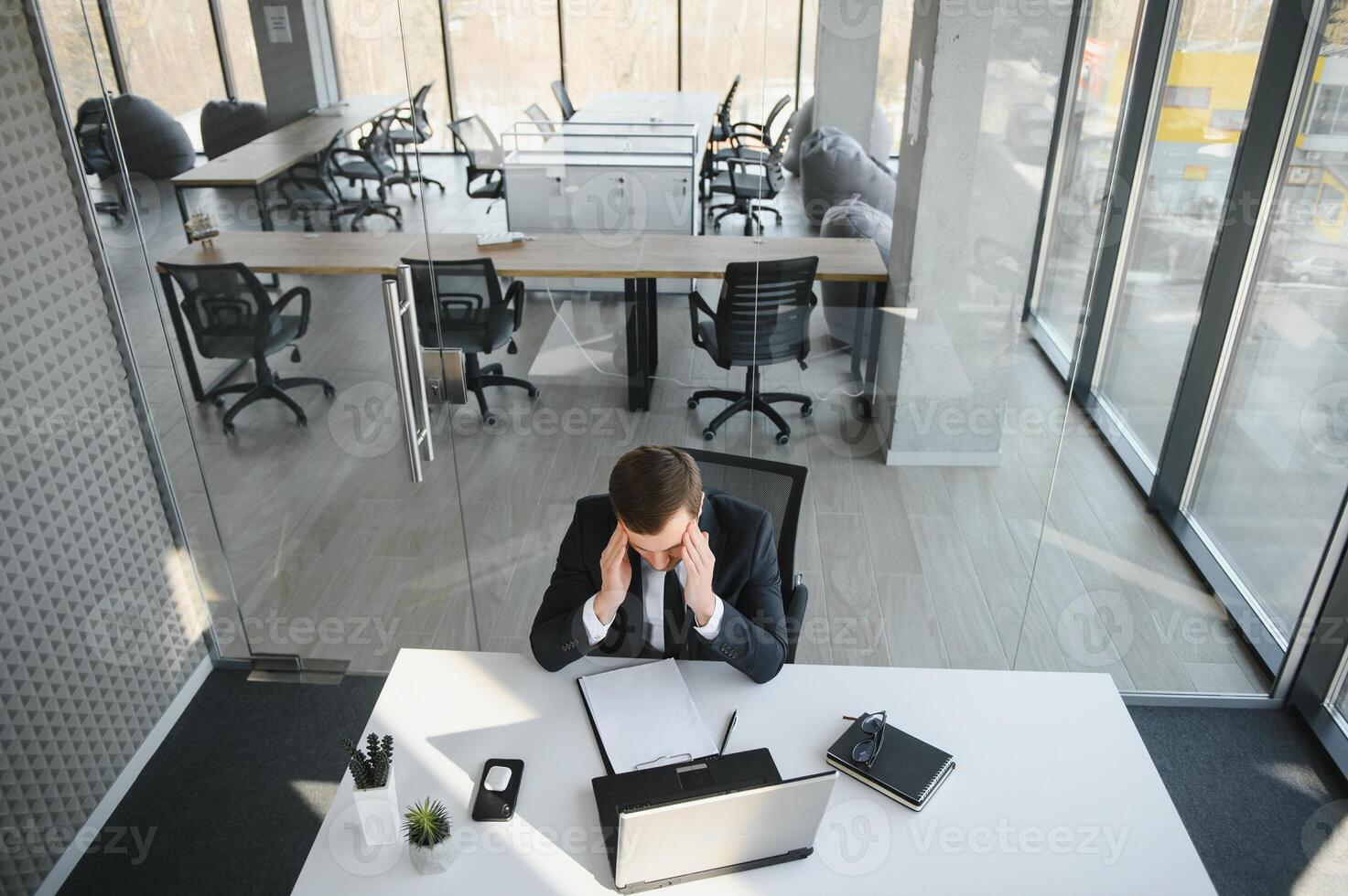 Young stressed handsome businessman working at desk in modern office shouting at laptop screen and being angry about financial situation, jealous of rival capabilities, unable to meet client needs photo