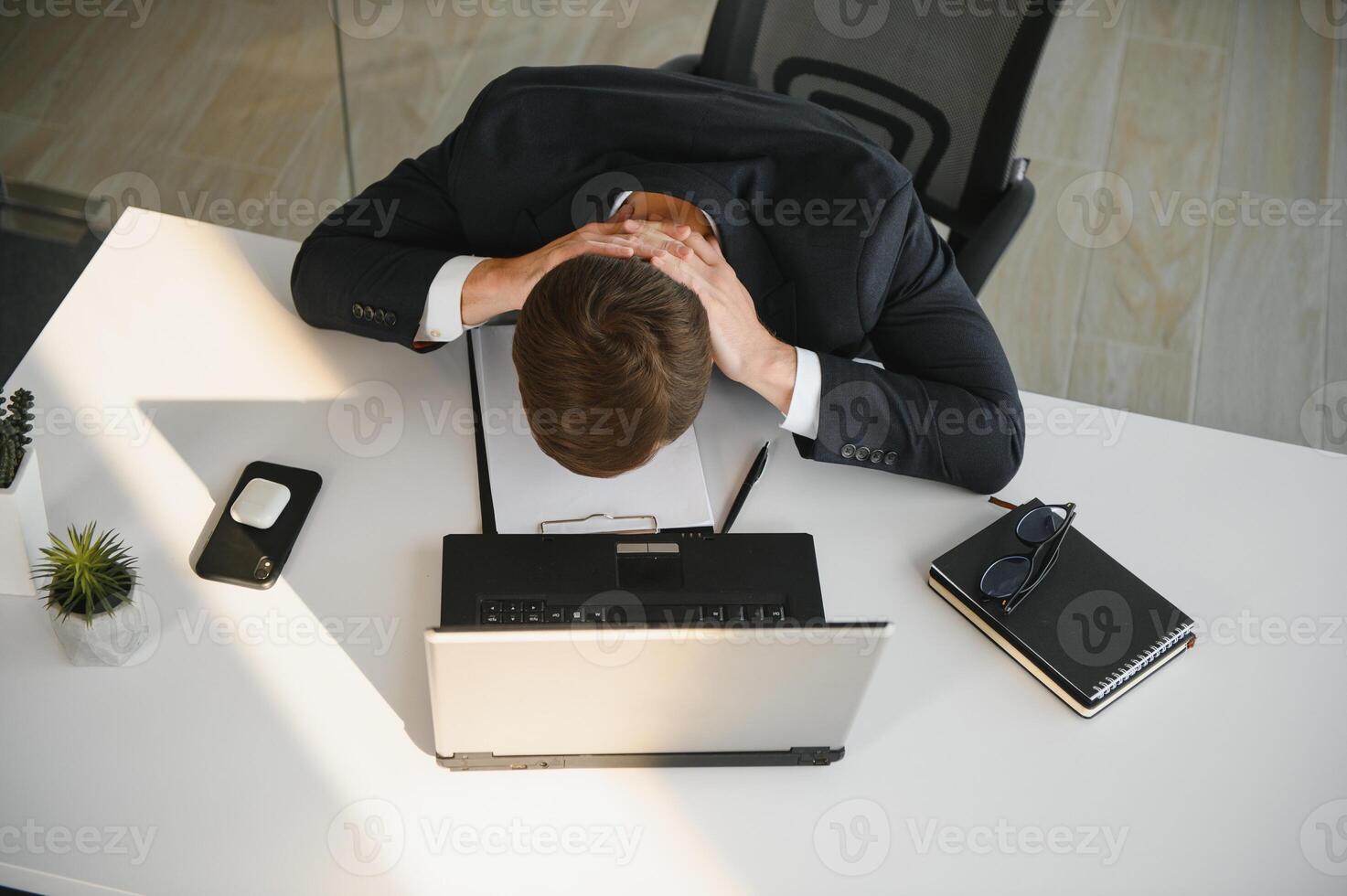 Depressed young businessman holding head in hands, has problem, a laptop on the desk. A guy made a mistake in a work photo