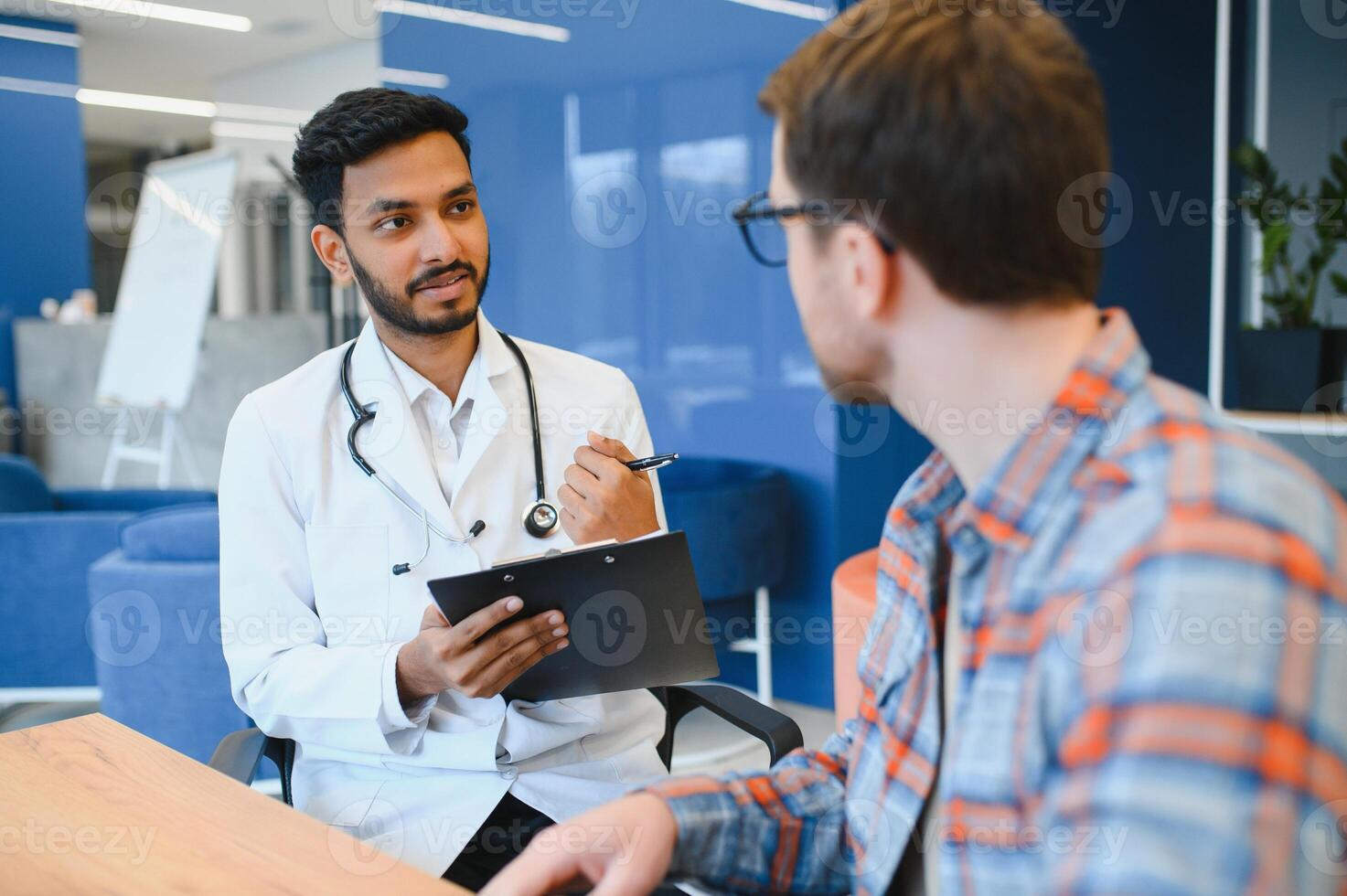 Indian doctor in white gown seeing patients in office. photo