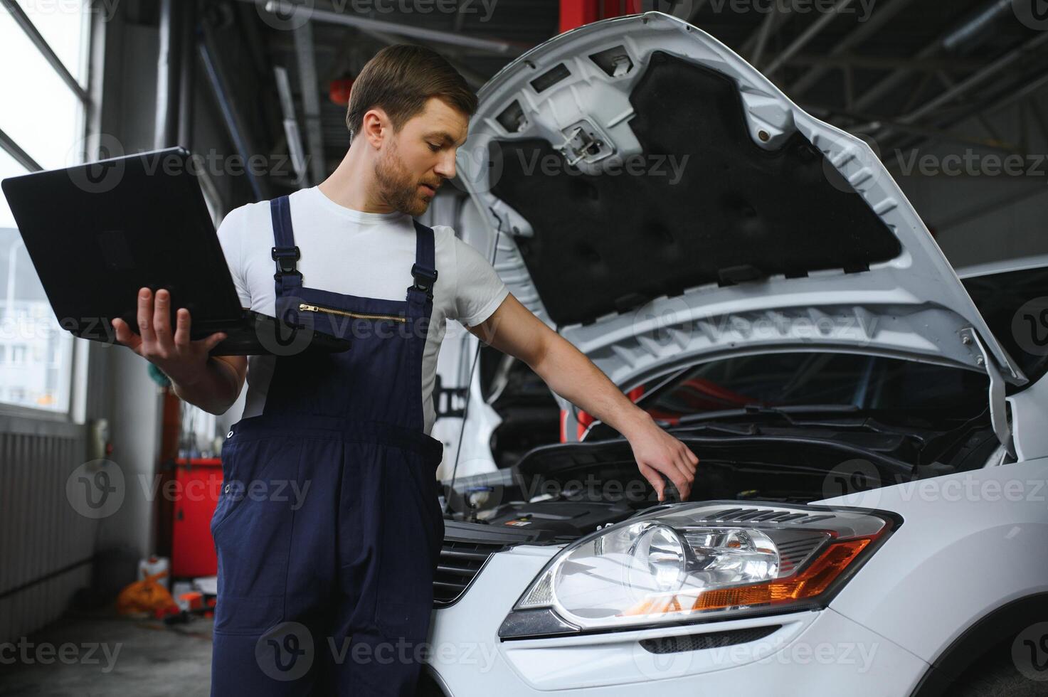 Mechanic man mechanic manager worker using a laptop computer checking car in workshop at auto car repair service center. Engineer young man looking at inspection vehicle details under car hood photo