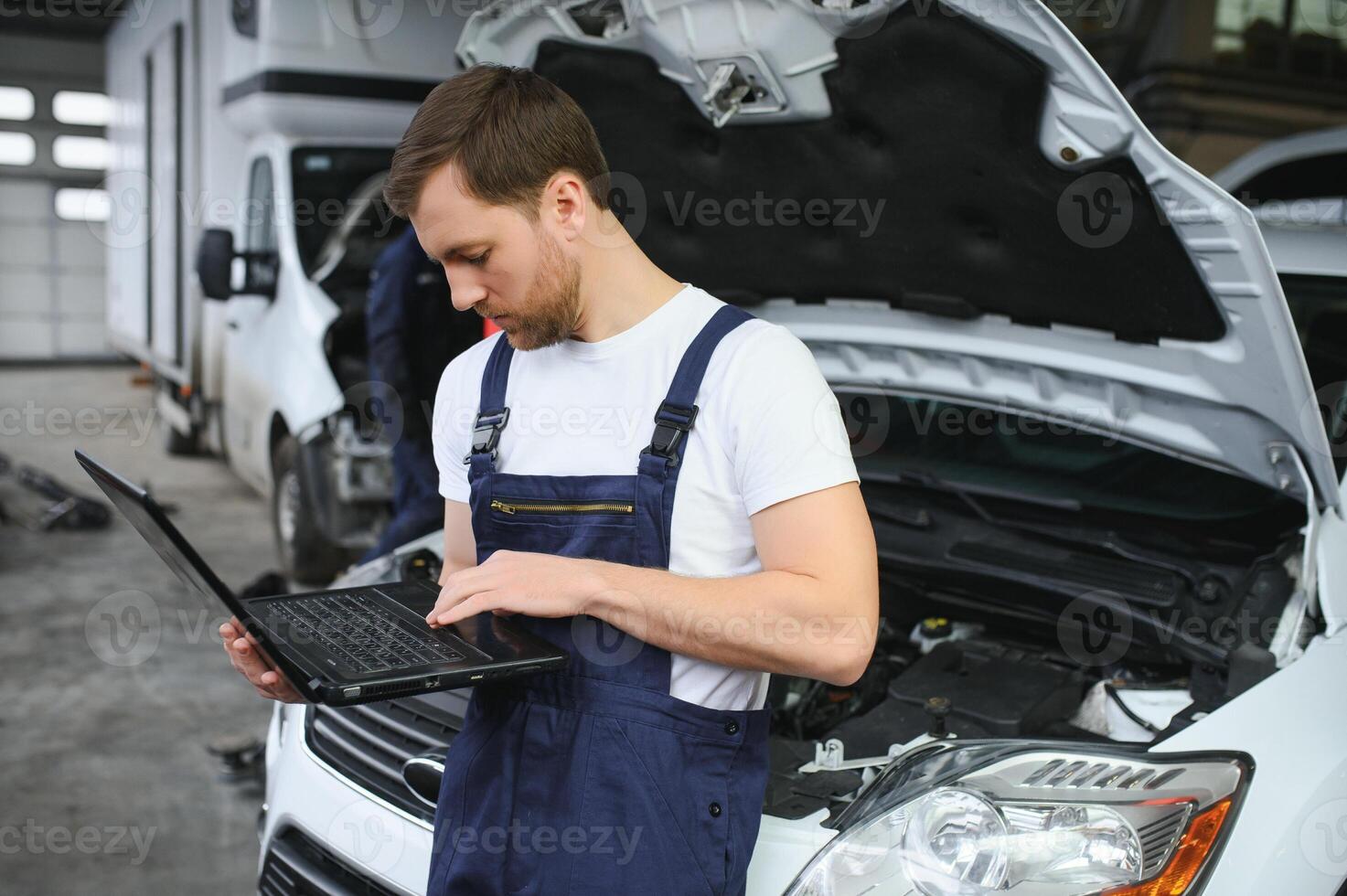 car mechanic using a computer laptop to diagnosing and checking up on car engines parts for fixing and repair photo