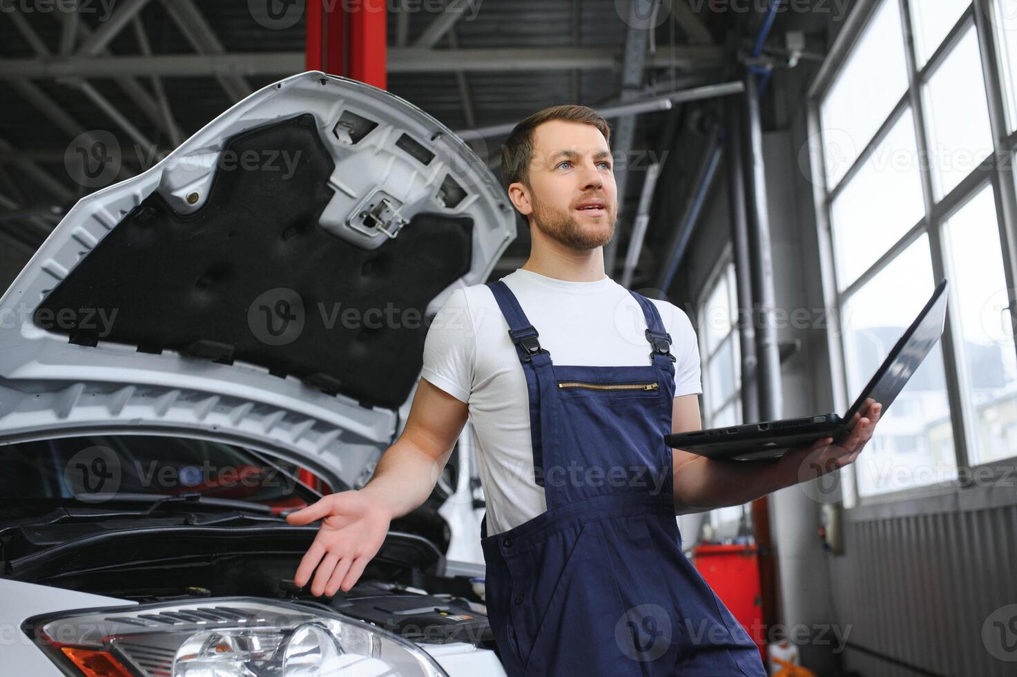 car mechanic using a computer laptop to diagnosing and checking up on car engines parts for fixing and repair photo