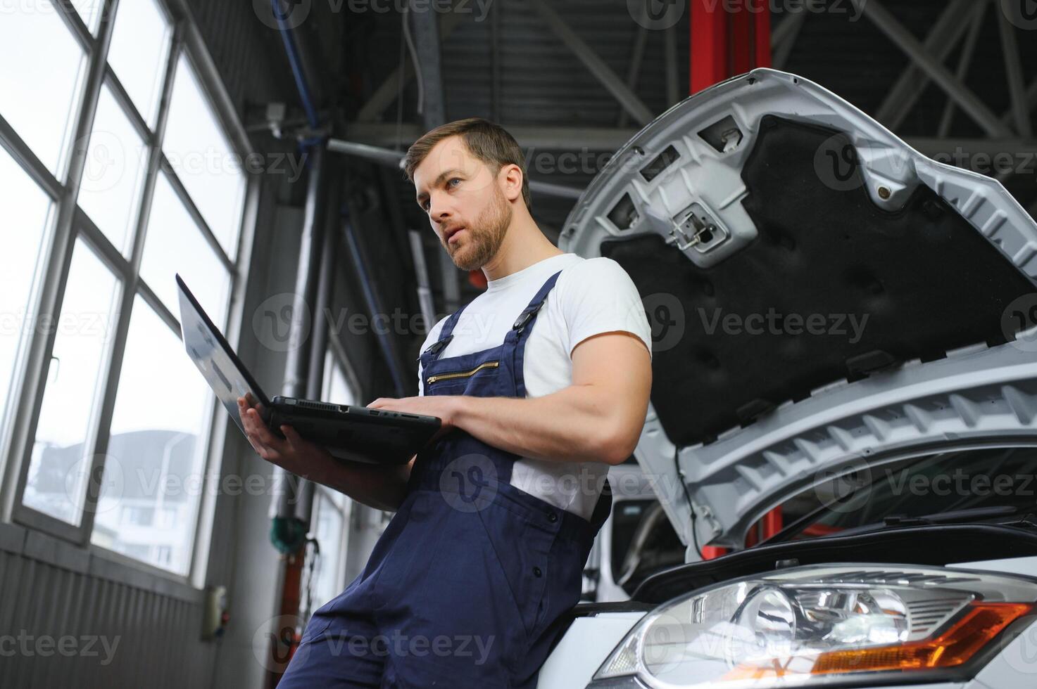Mechanic man mechanic manager worker using a laptop computer checking car in workshop at auto car repair service center. Engineer young man looking at inspection vehicle details under car hood photo