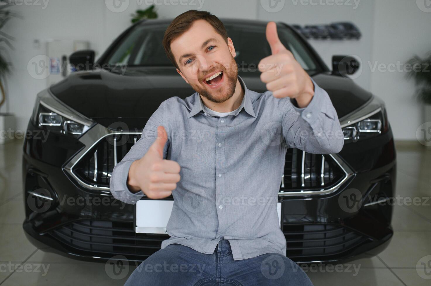 Emotional handsome guy raising hand up and smiling at camera. Rich man buying auto at luxury dealership salon photo
