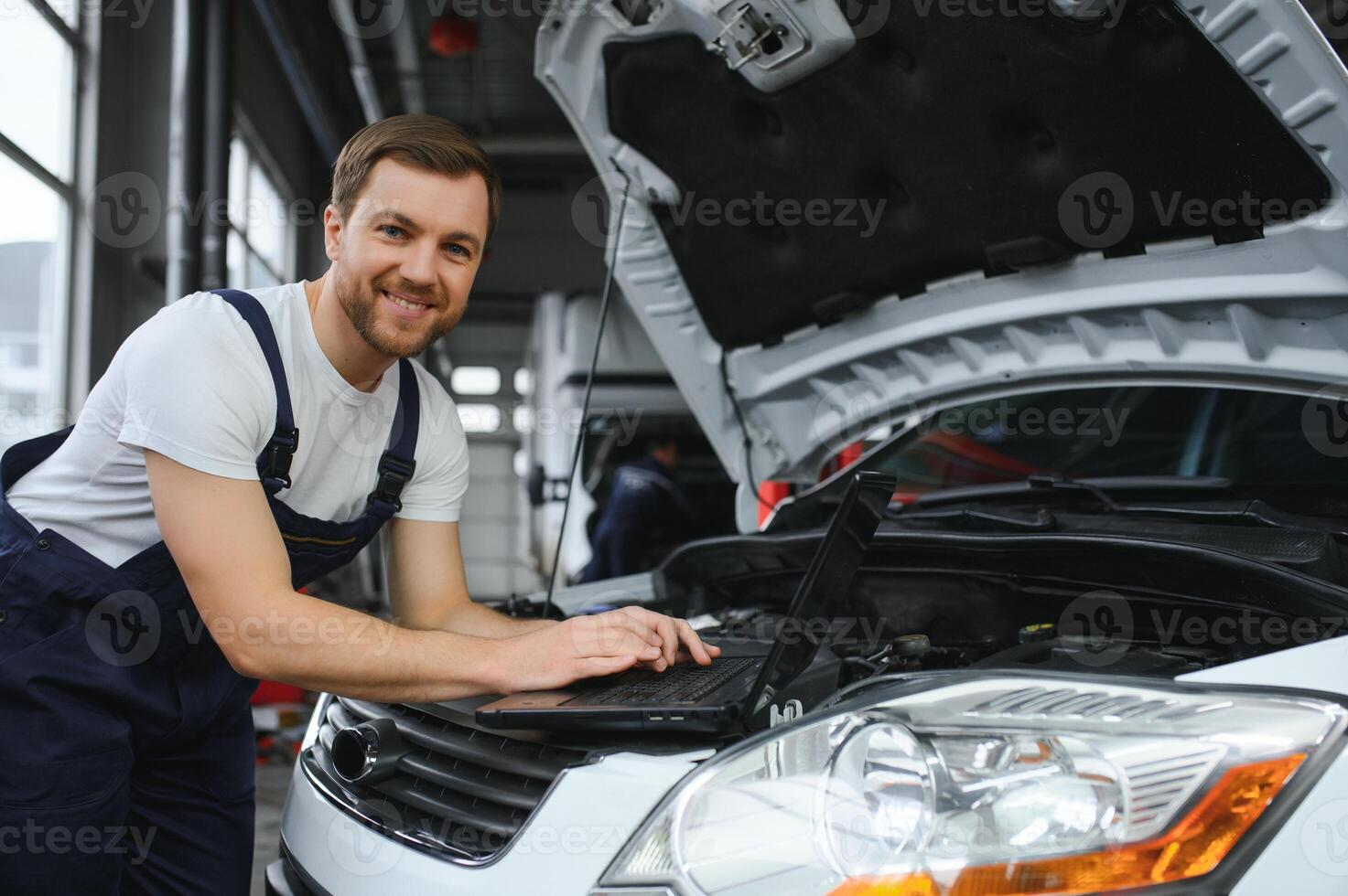 Mechanic man mechanic manager worker using a laptop computer checking car in workshop at auto car repair service center. Engineer young man looking at inspection vehicle details under car hood photo