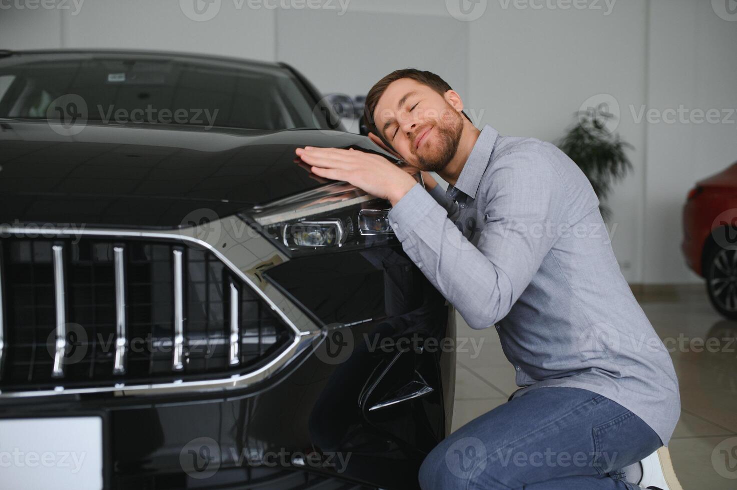 Visiting car dealership. Handsome bearded man is stroking his new car and smiling. photo