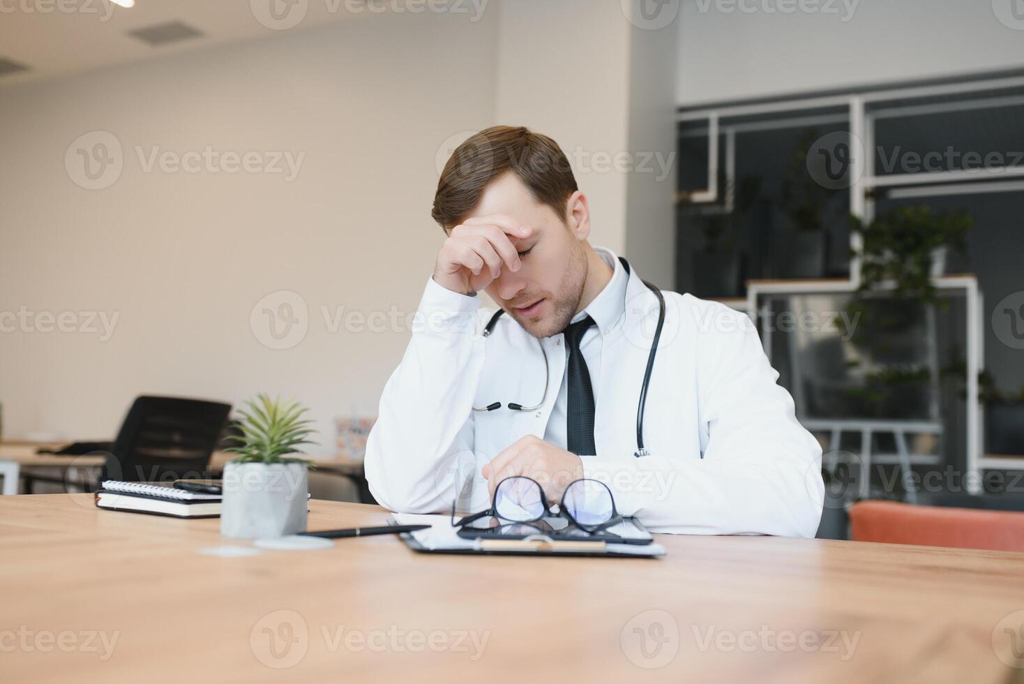 Stressed male doctor. Mid adult male doctor working long hours. Overworked doctor in his office. Not even doctors are exempt from burnout . photo