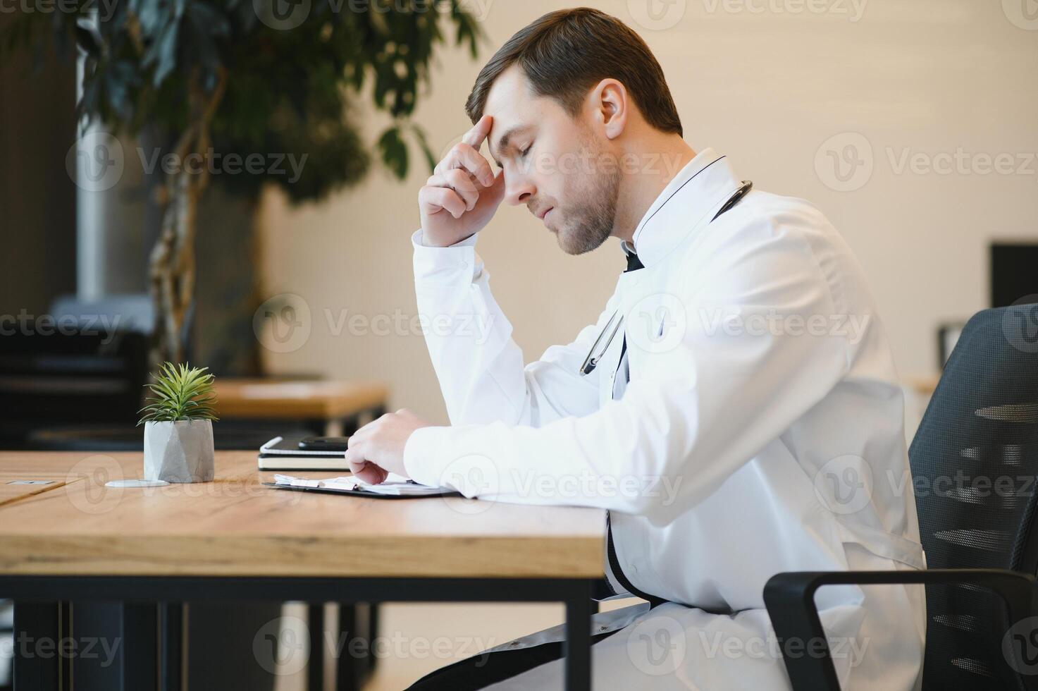Stressed male doctor. Mid adult male doctor working long hours. Overworked doctor in his office. Not even doctors are exempt from burnout . photo