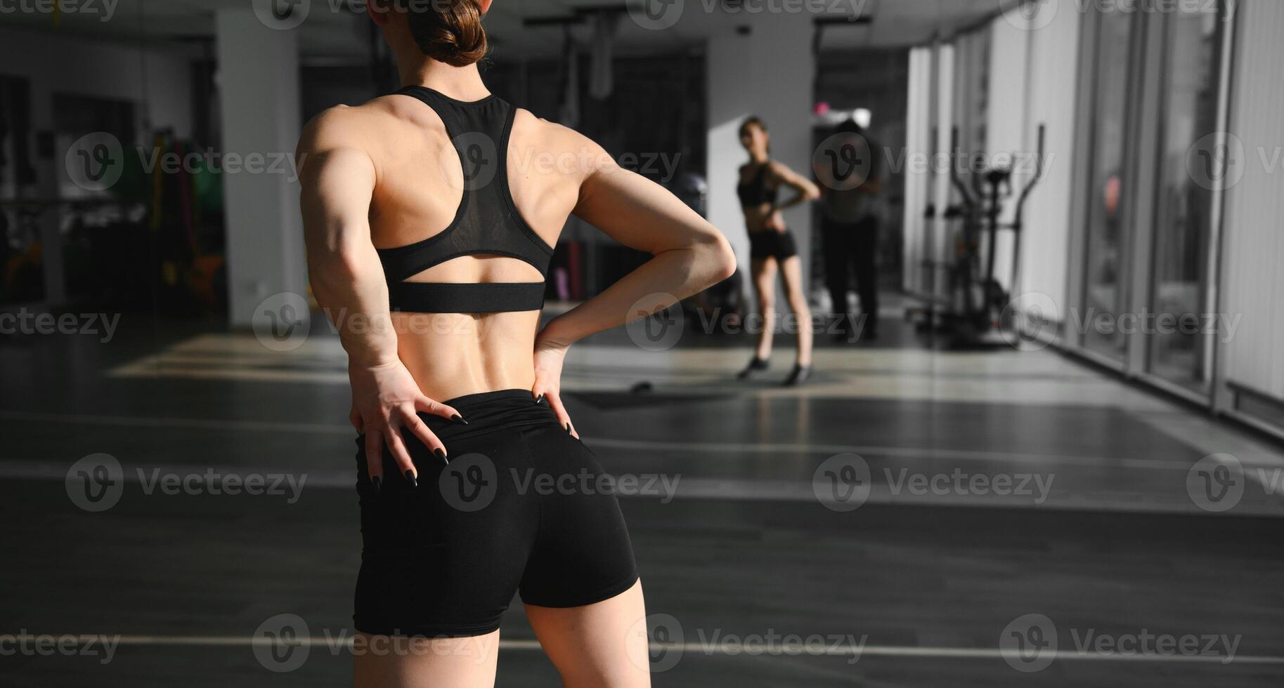 Rear view of young sporty woman in sports clothes stretching arms against grey background, copy space photo