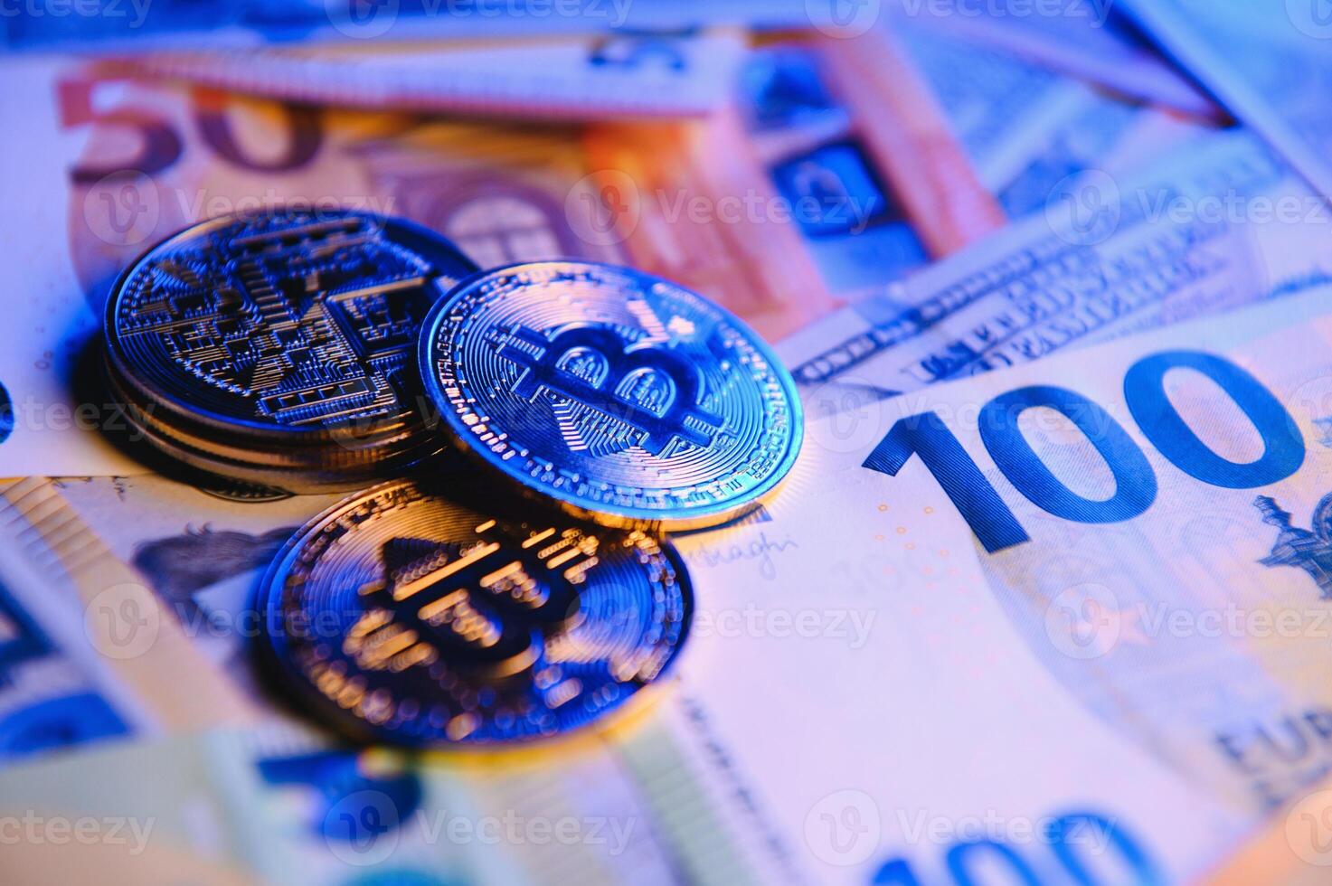 Close up heap of golden bitcoin physical coins on top of Euro, dollar banknotes background, high angle view, selective focus photo