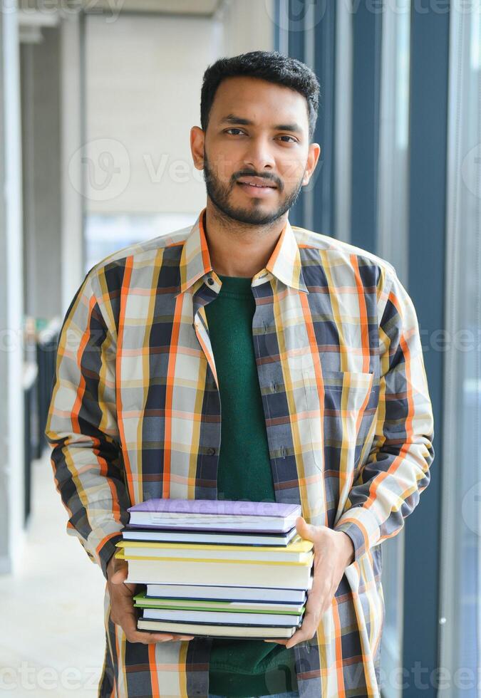 Young indian student boy reading book studying in college library with bookshelf behind. working on assignment or project photo