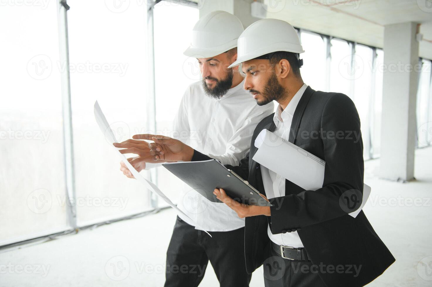 Multiracial male coworkers in hardhats discussing project on construction site photo