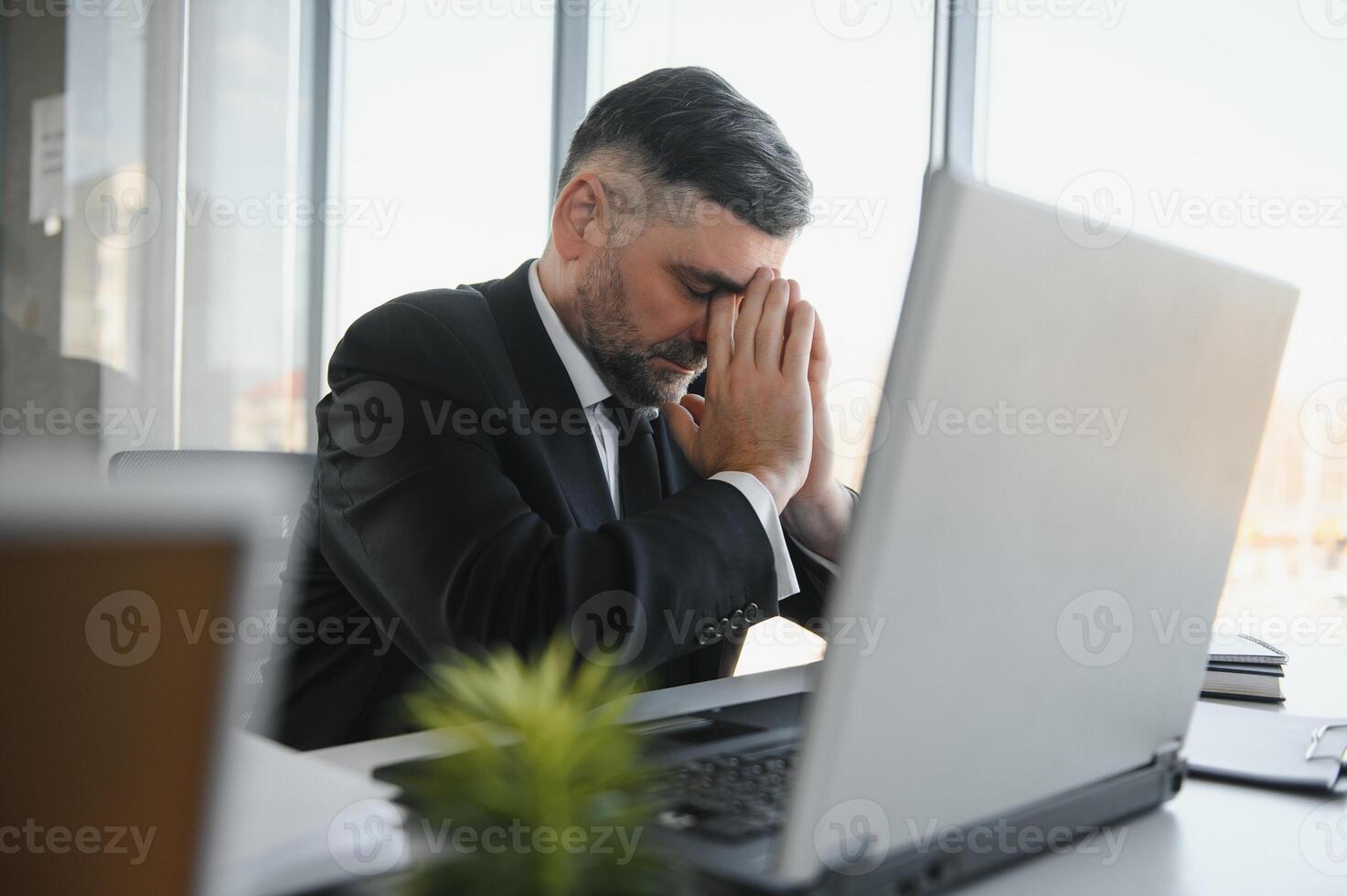 Tired stressed office worker sitting at desk and thinking, he is rubbing his eyes and feeling exhausted. photo