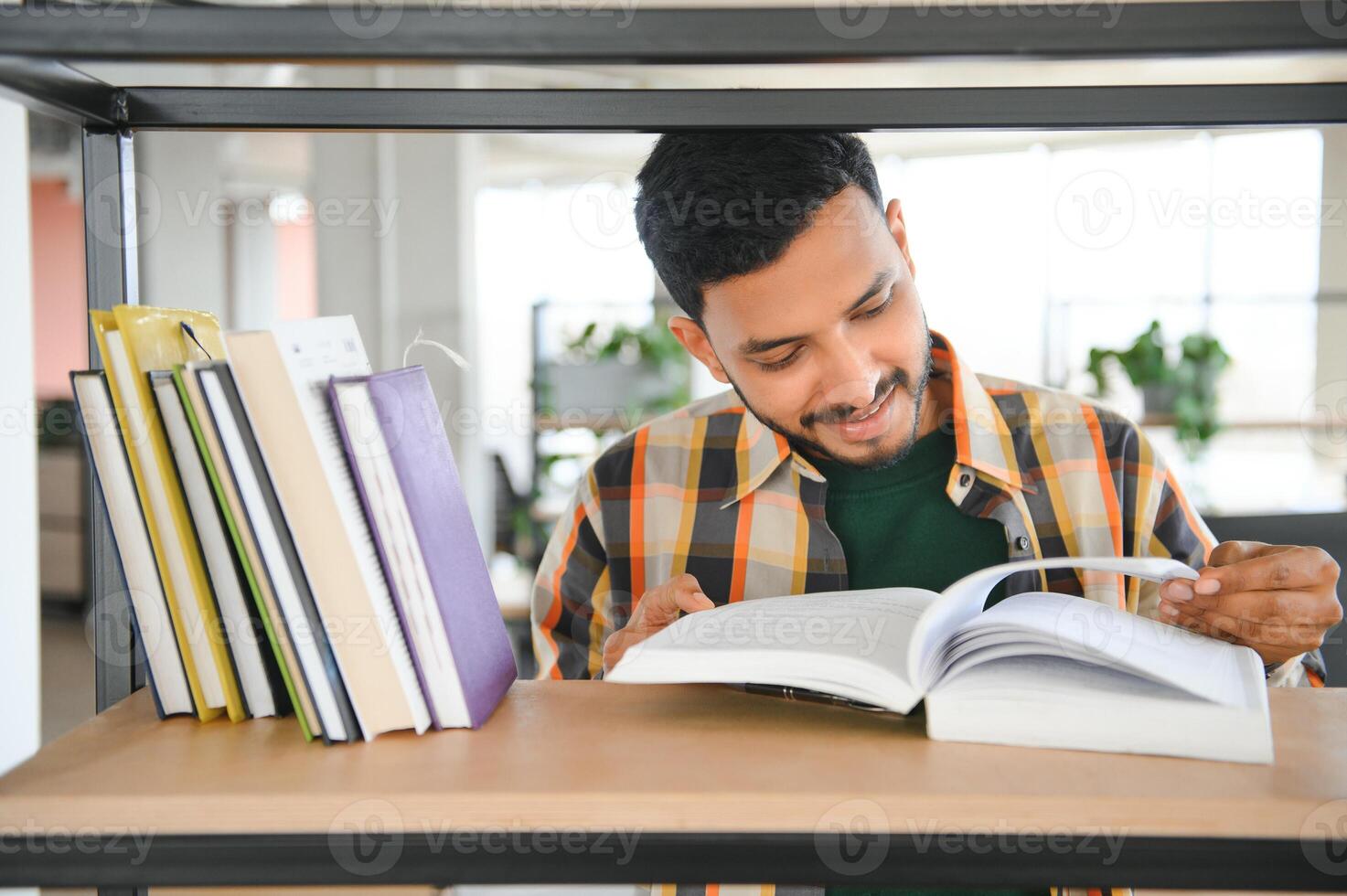Happy smart indian or arabian guy, mixed race male, university student, stands in the library against the background of bookshelves photo
