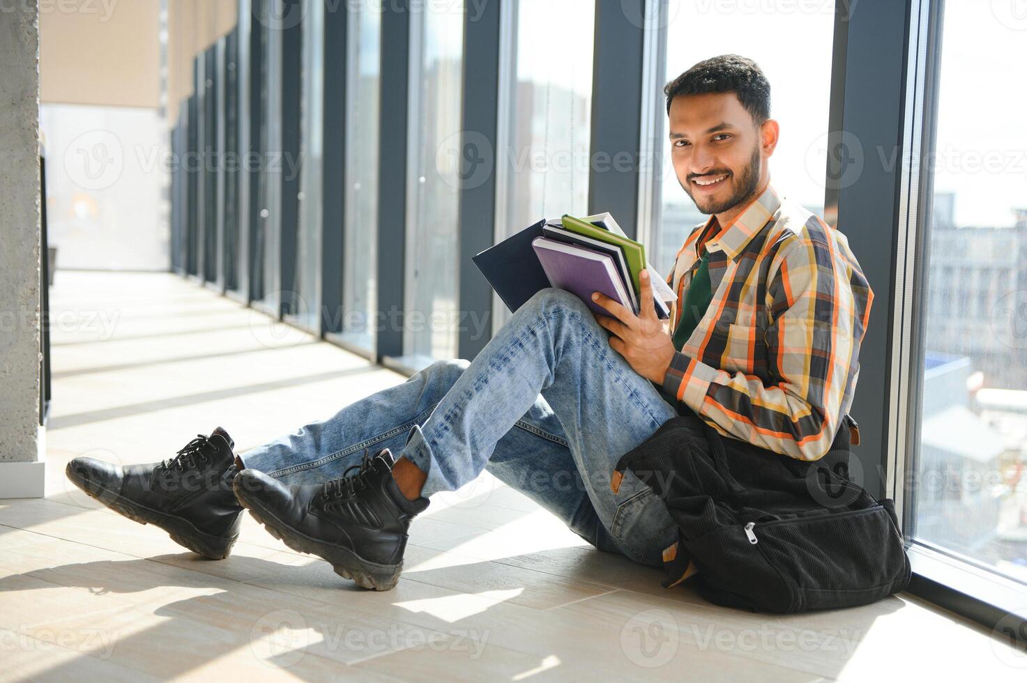 Young indian student boy reading book studying in college library with bookshelf behind. working on assignment or project photo
