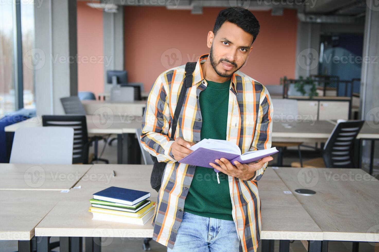 Young indian student boy reading book studying in college library with bookshelf behind. working on assignment or project photo