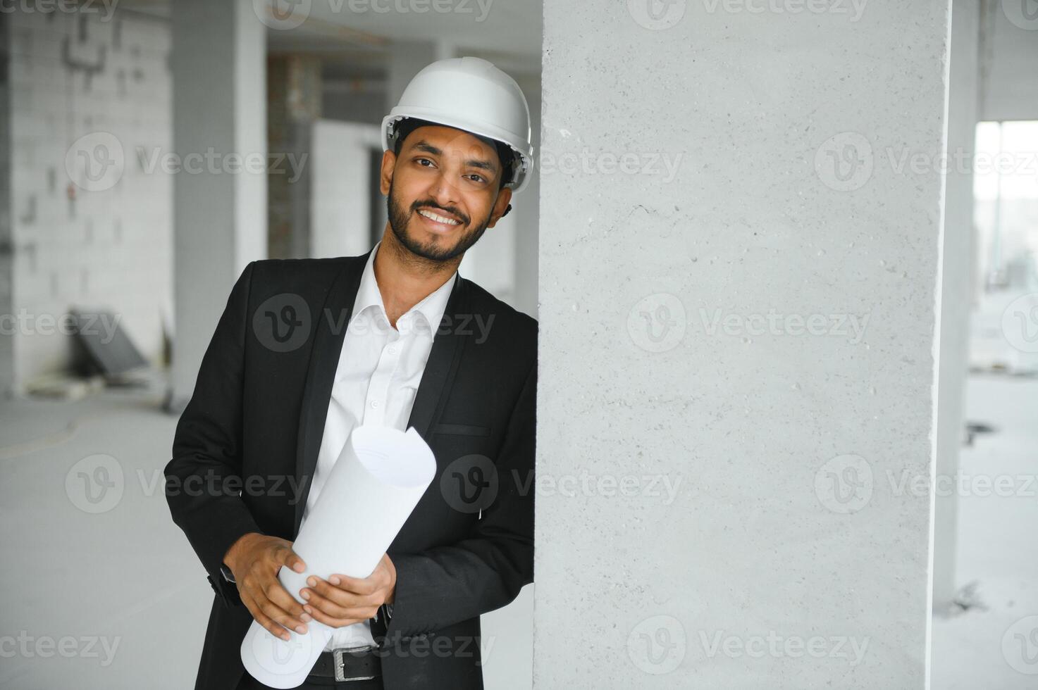 Indian construction site manager standing wearing helmet, thinking at construction site. Portrait of mixed race manual worker or architect. photo