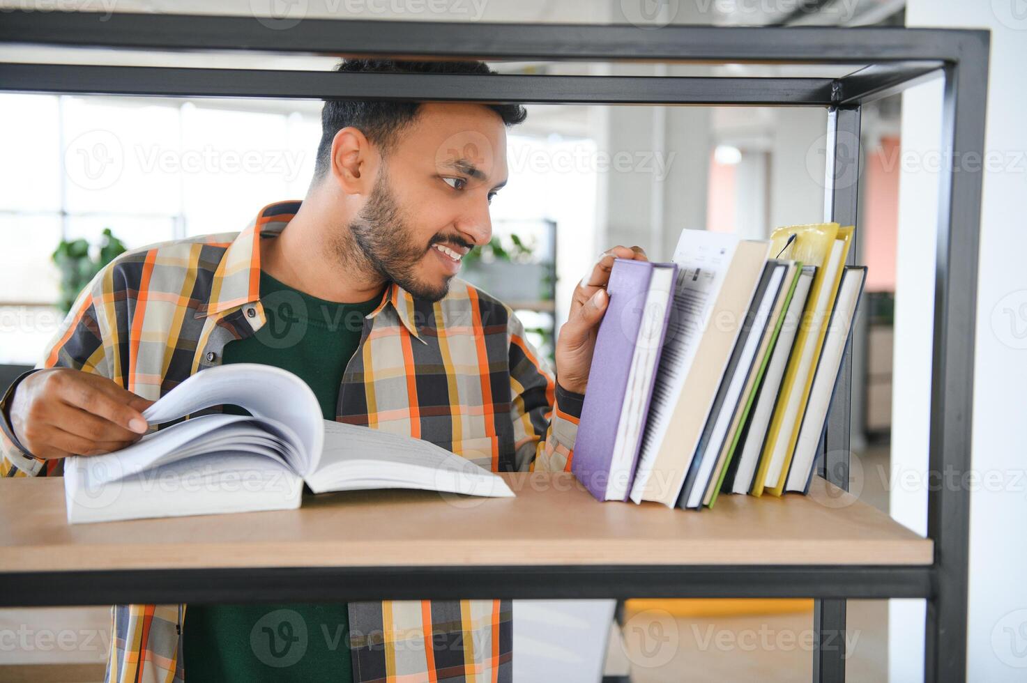 Happy smart indian or arabian guy, mixed race male, university student, stands in the library against the background of bookshelves photo