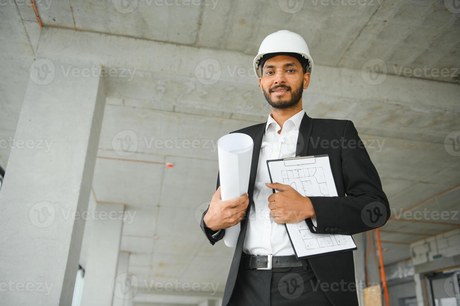 Indian construction site manager standing wearing helmet, thinking at construction site. Portrait of mixed race manual worker or architect. photo